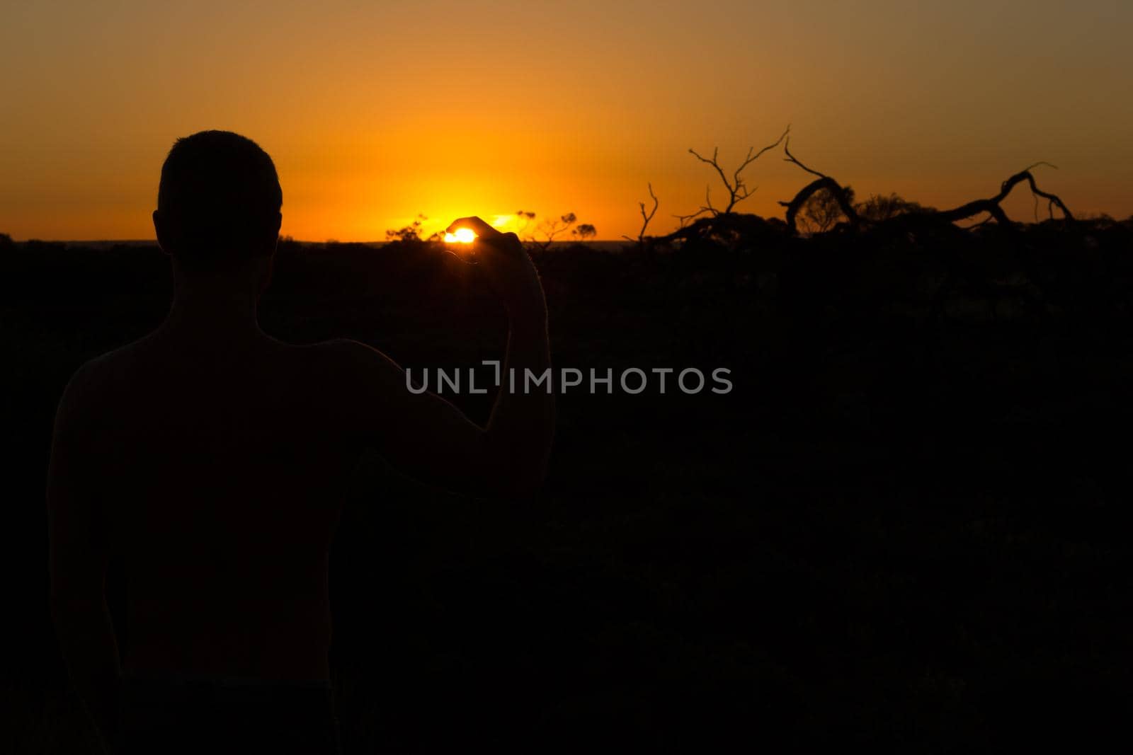 silhouette of young man holding sun during sunset in outback South Australia, Australia