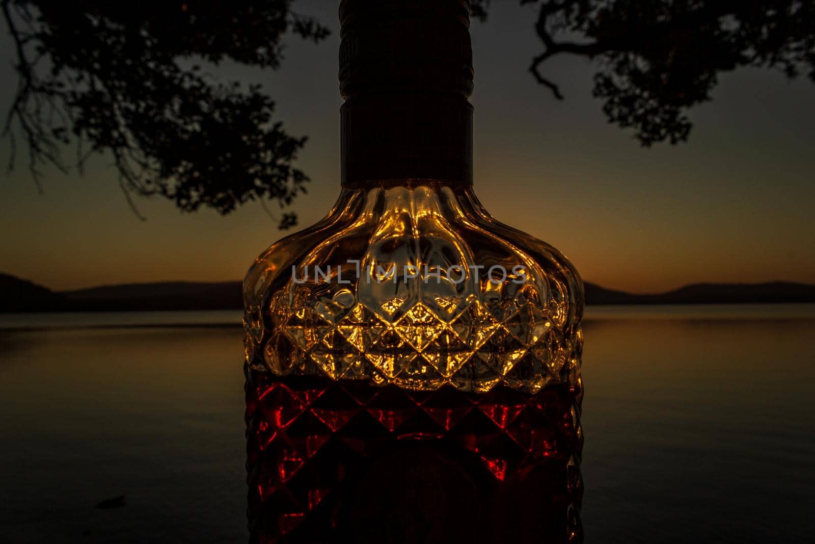 beautiful rum bottle full with rum holding in front of a sunset over Watson Taylors Lake at Crowdy Bay National Park, New South Wales, Australia by bettercallcurry