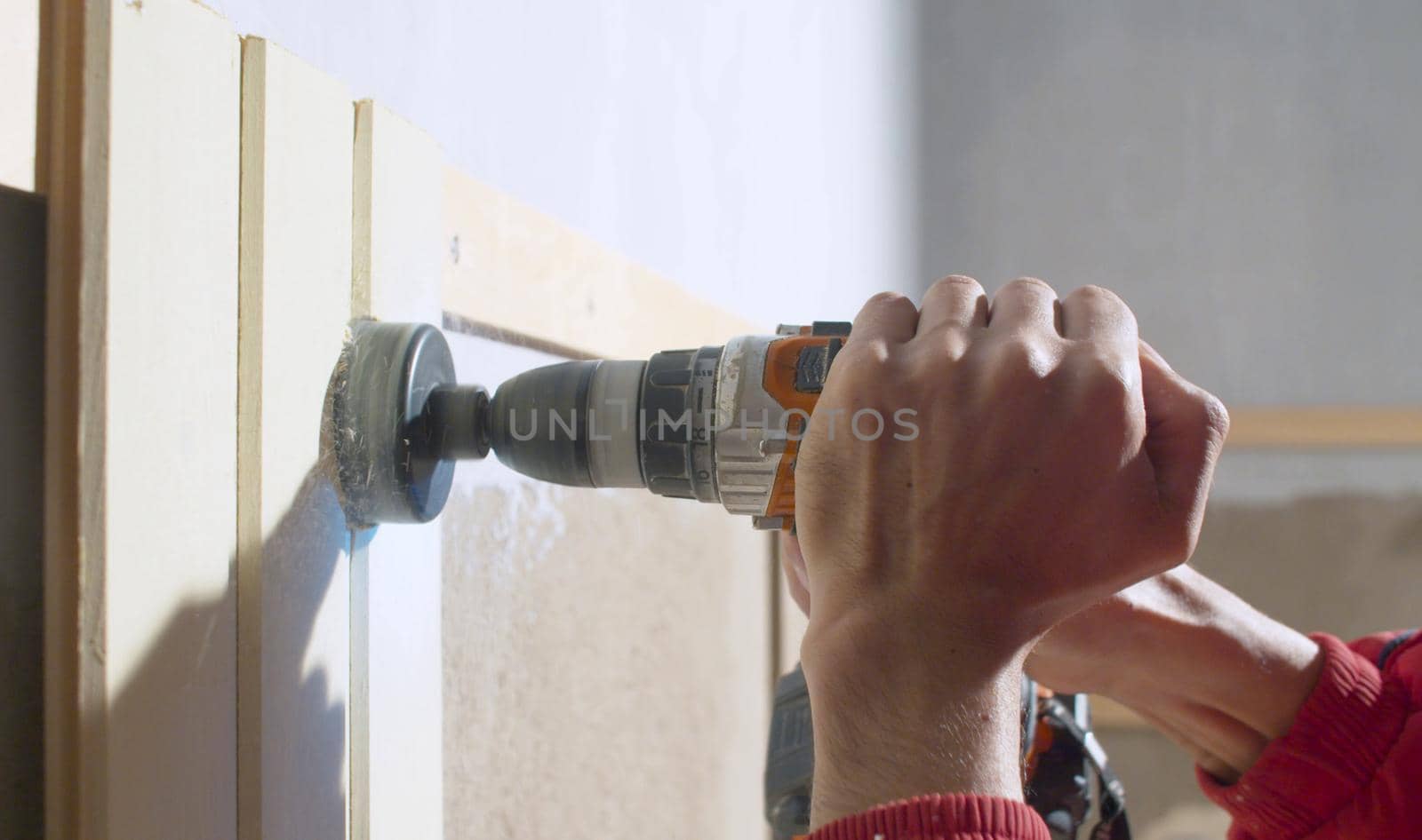 The builder cuts a round hole in the wooden board for an electrical switch using a special tool and a drill