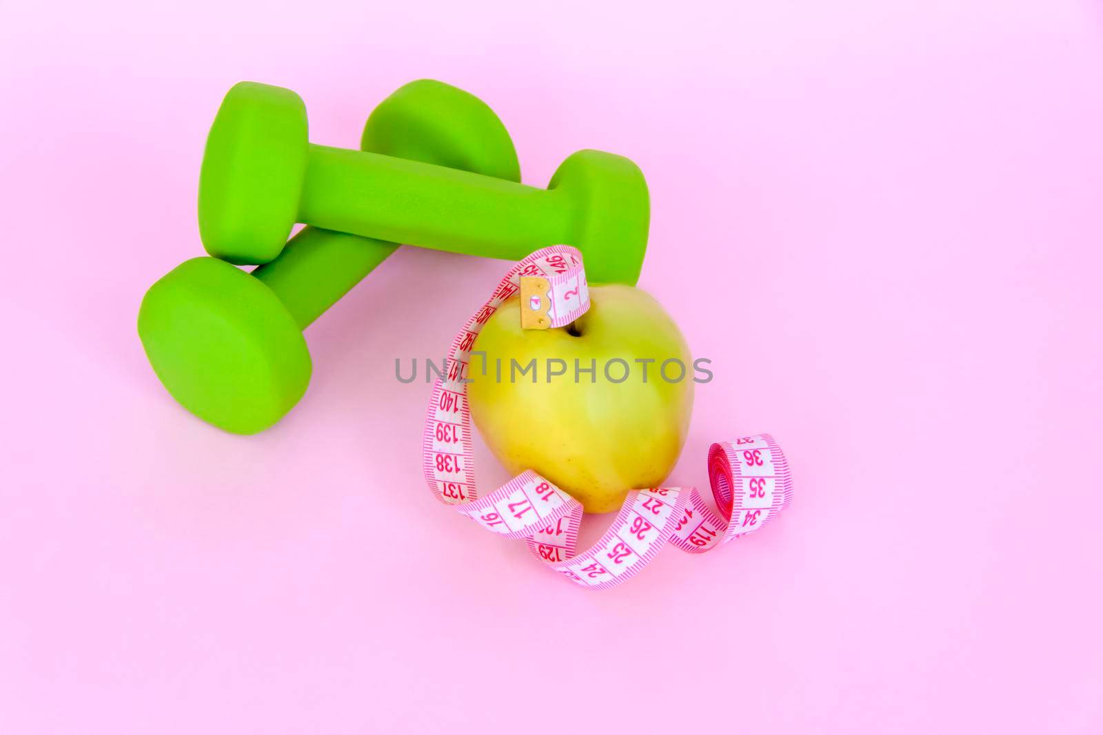 A green apple, and a centimeter measuring tape on a pink background. Sports, sports nutrition, healthy eating, diet. Space for the text. Exercise, lose weight 