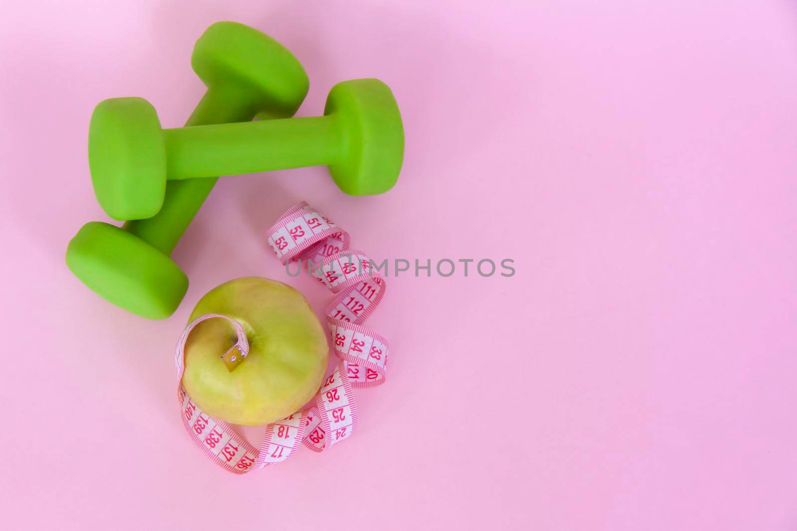 A green apple, and a centimeter measuring tape on a pink background. Sports, sports nutrition, healthy eating, diet. Space for the text. Exercise, lose weight