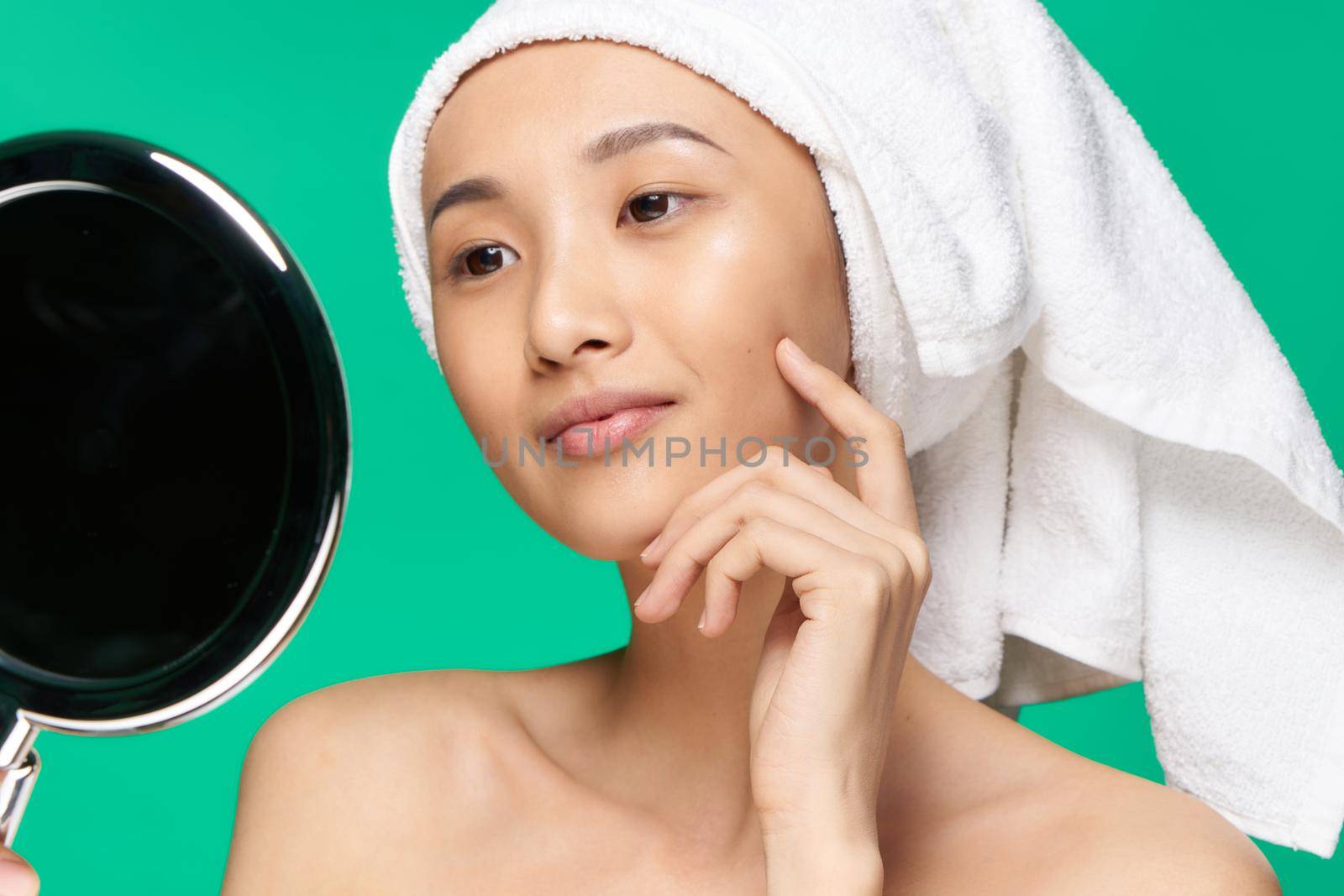 pretty smiling woman with a towel on her head looks at the mirror clean skin after a shower Green background by SHOTPRIME