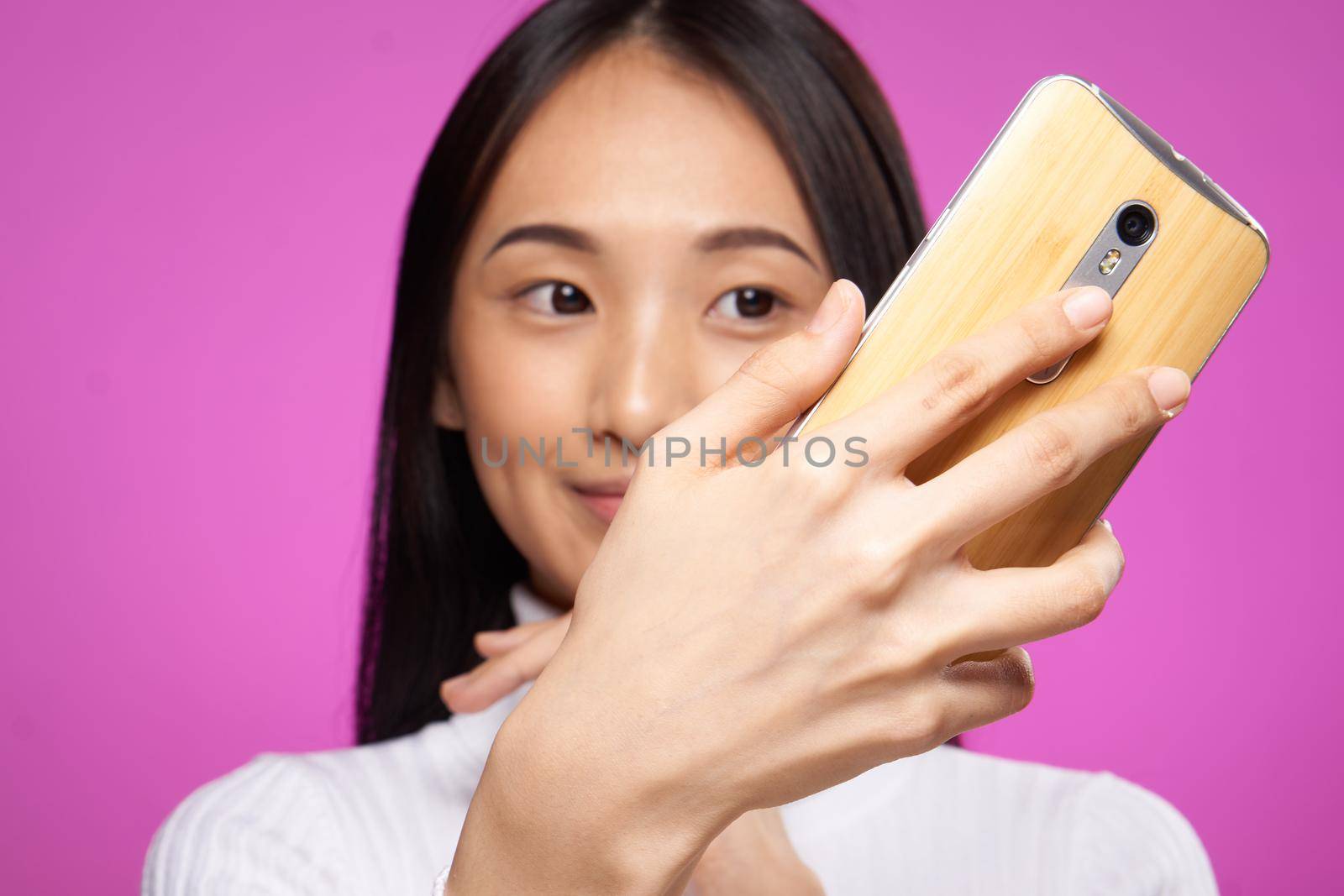 pretty asian woman with a phone in her hands looking at the screen close-up pink background. High quality photo