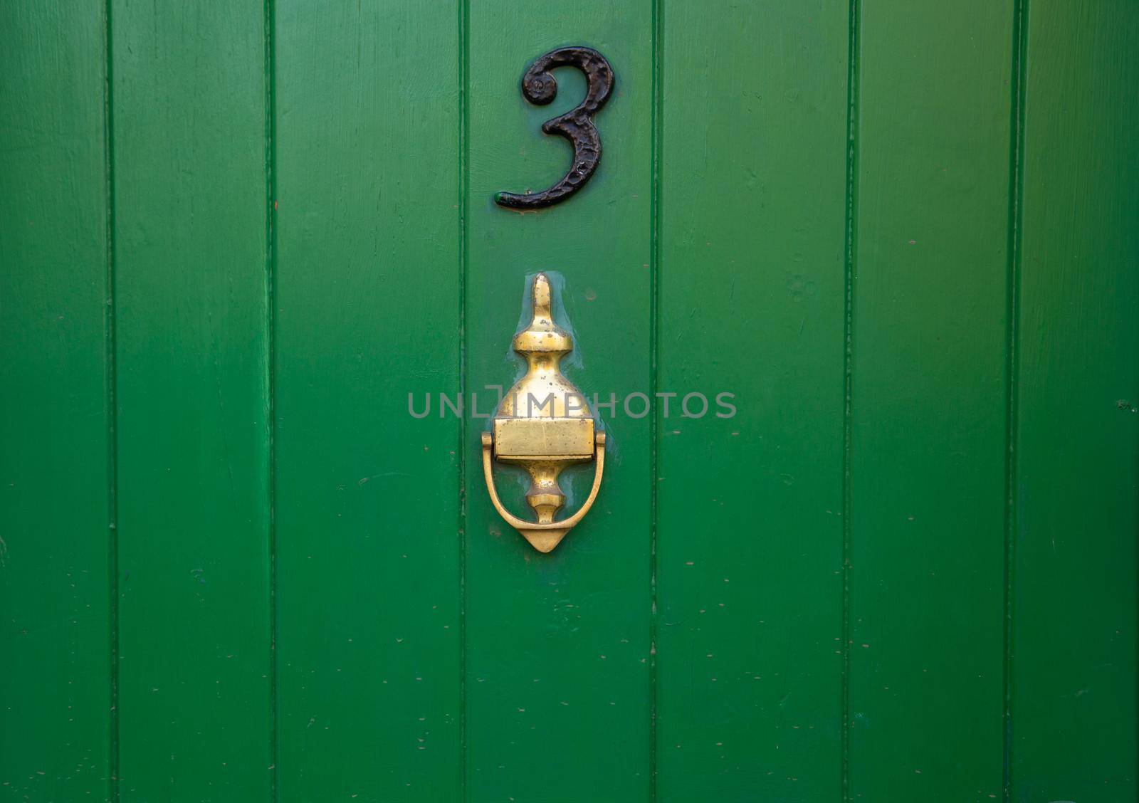 House number 3, green wooden front door with gold brass metal door knocker. Old antique painted door with knocker. UK, Suffolk