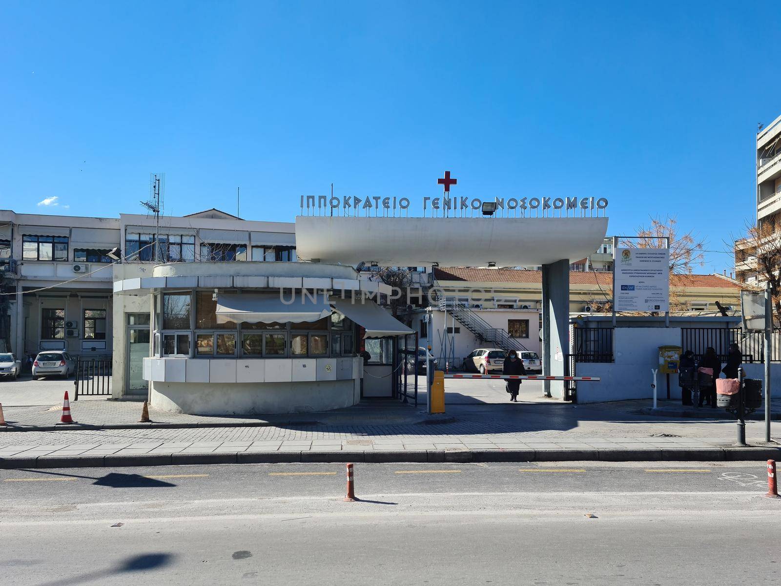 Day view of north gate facade of Hellenic public clinic with logo and red cross above.