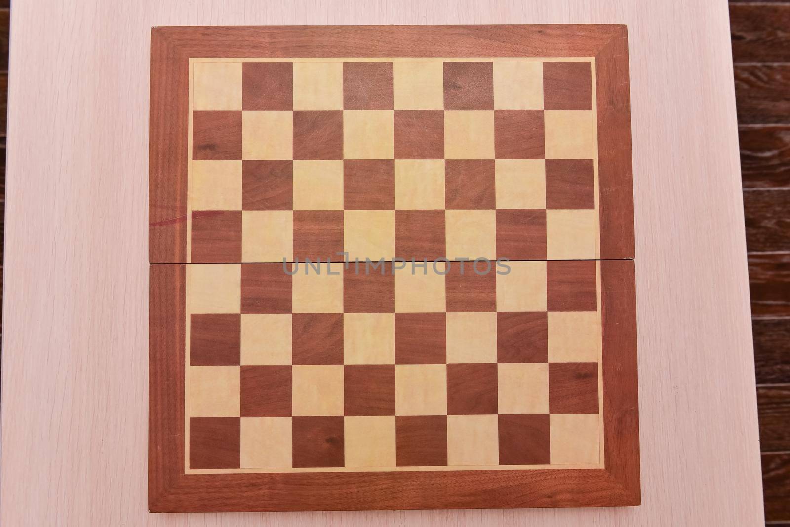 Top view on wooden chess board on light wooden table background.