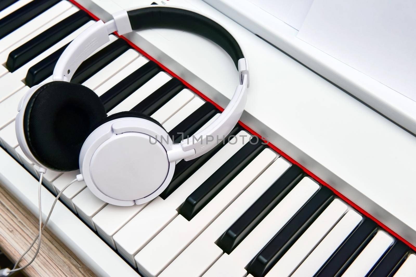 white headphones lie on the keyboard of the electronic piano.