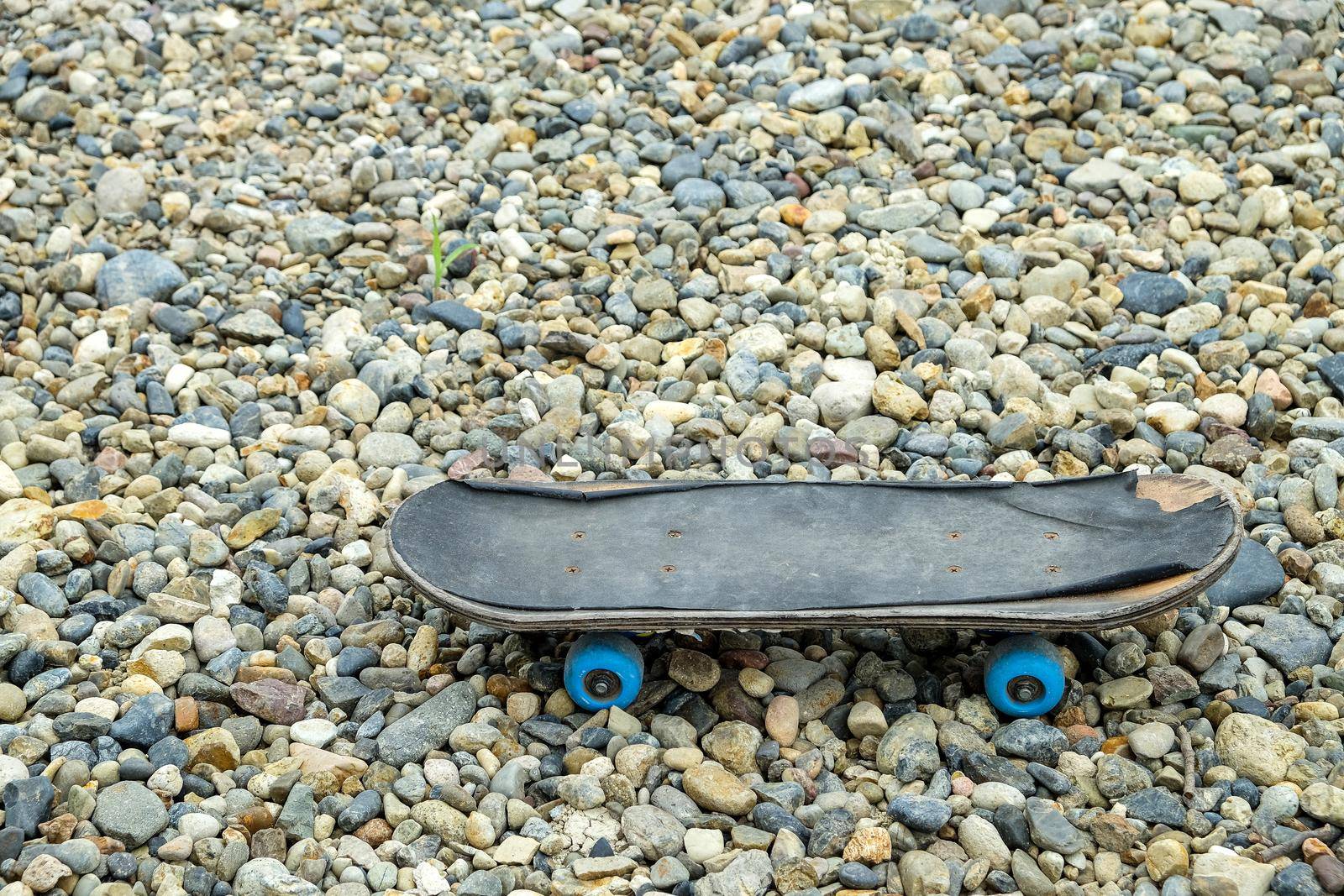 old skateboard stands on small colored pebbles.