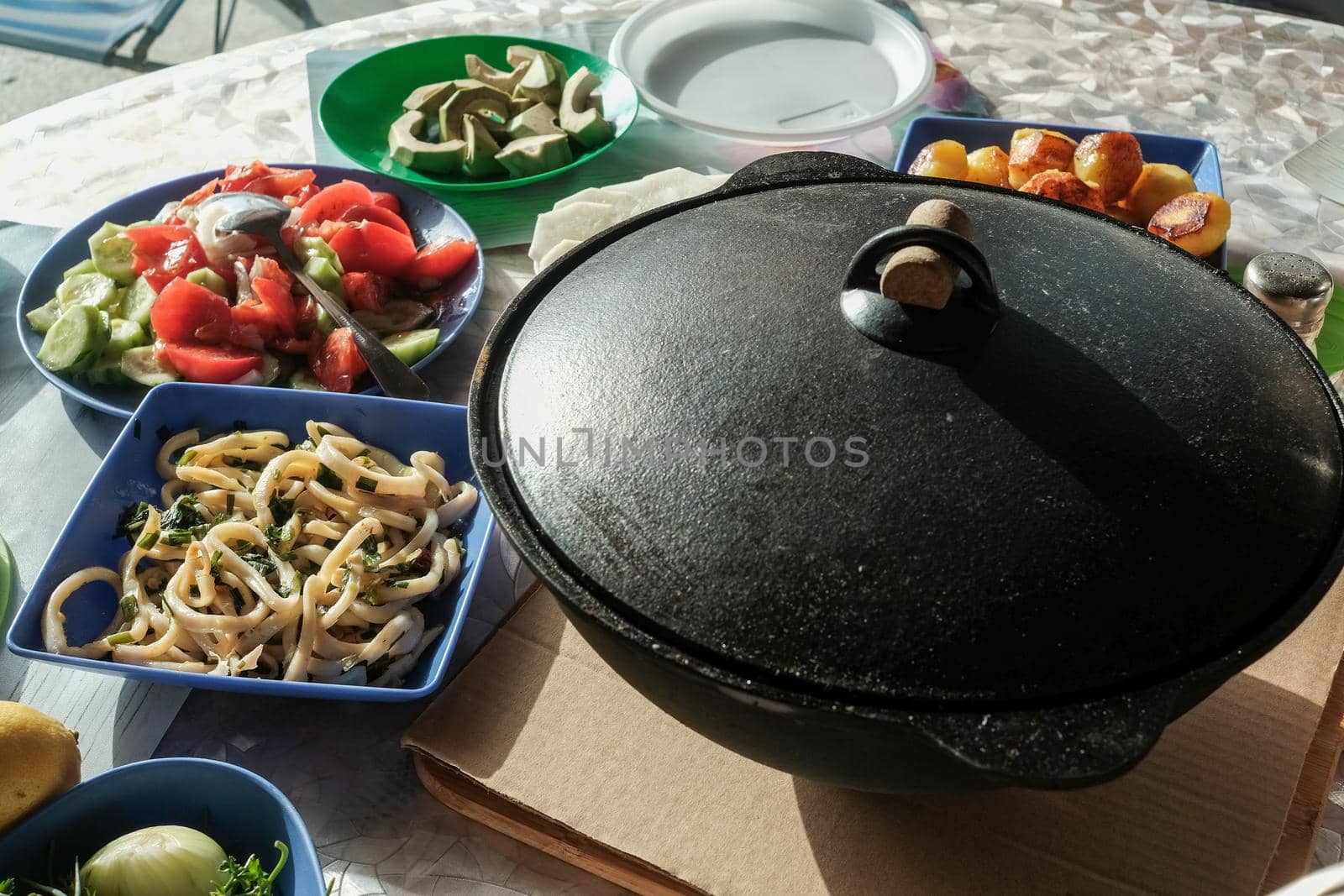 Seafood pilaf in an old cast iron cauldron. table with vegetable dishes.