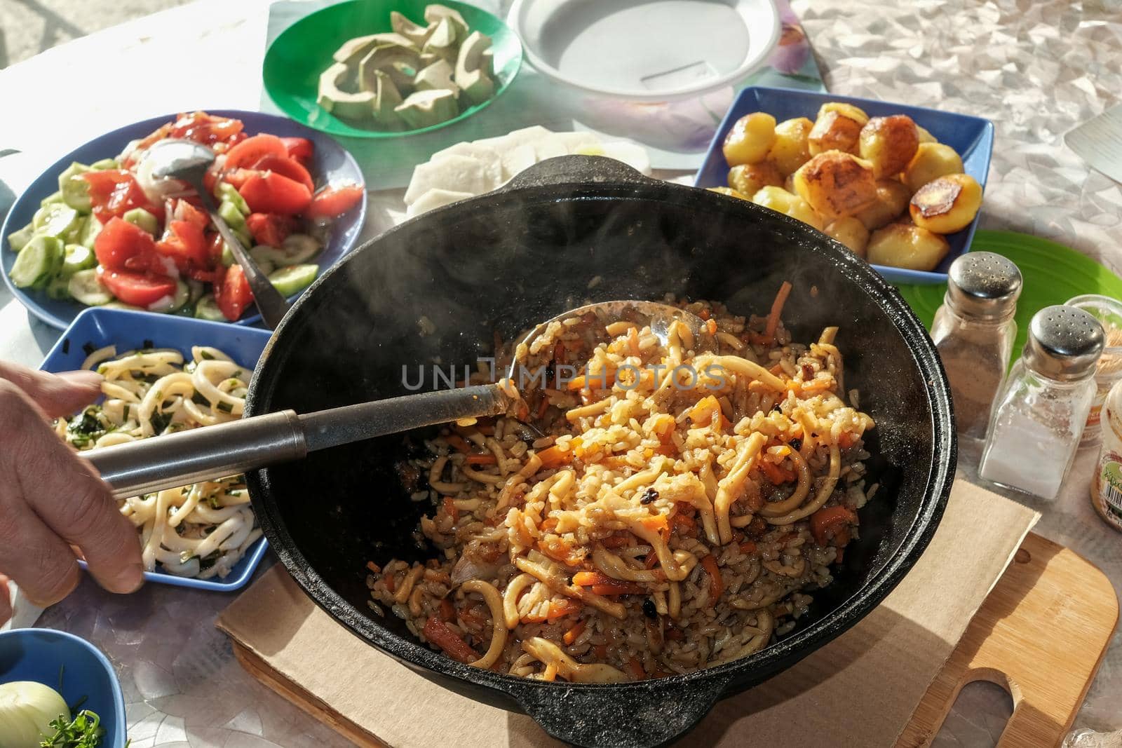 Seafood pilaf in an old cast iron cauldron. table with vegetable dishes.