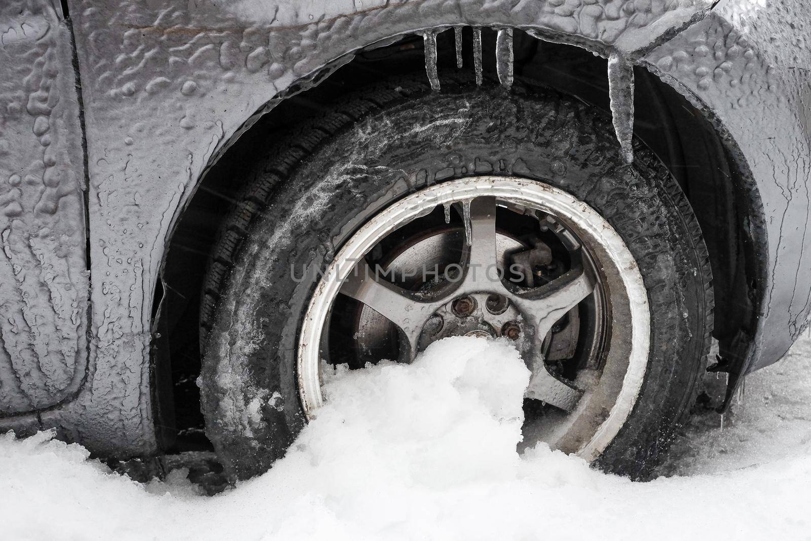 Ice buildup and icicles on a car and close-up of a frozen wheel.