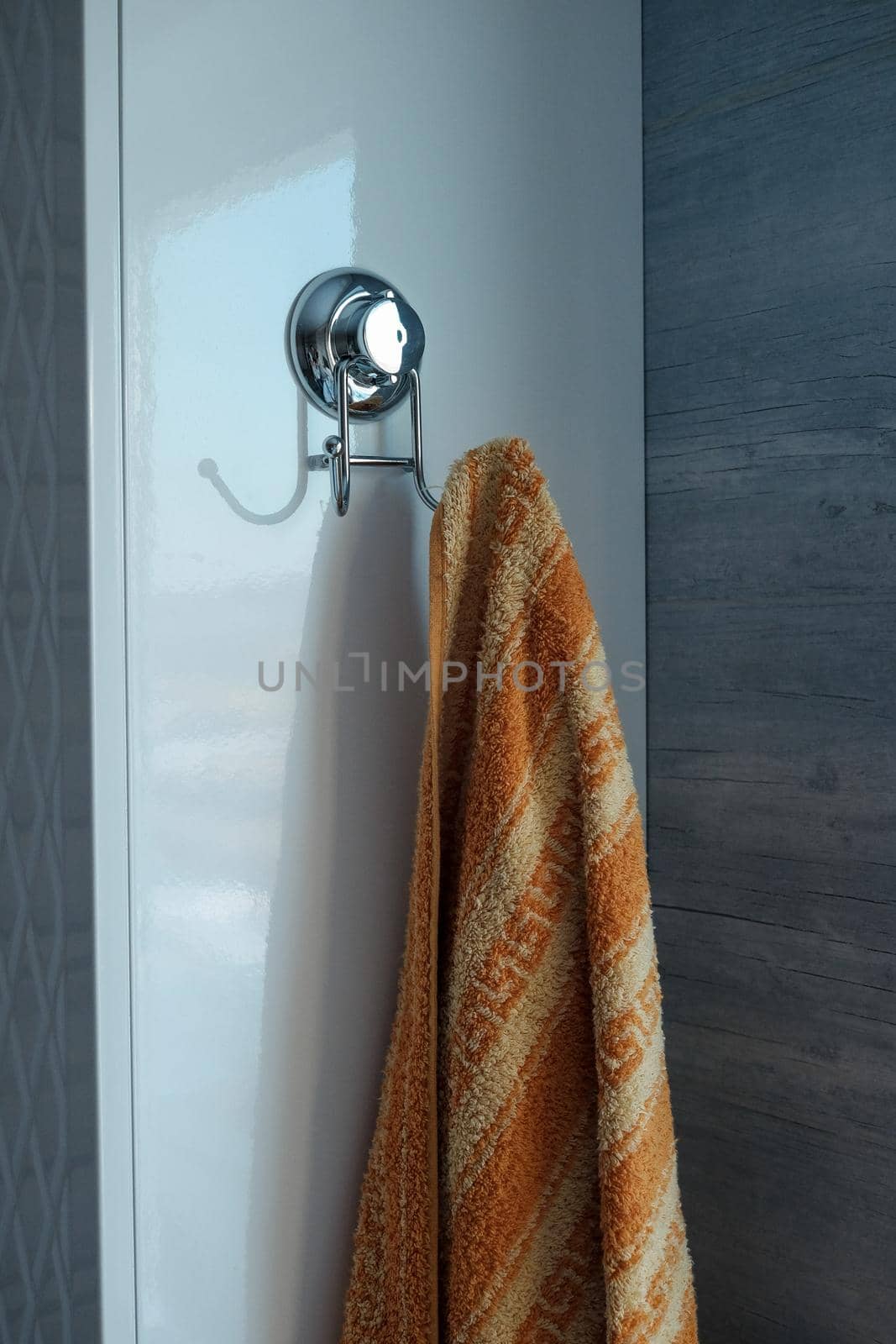 chrome hook-hanger on tiles with hanging towel in bathroom close-up.