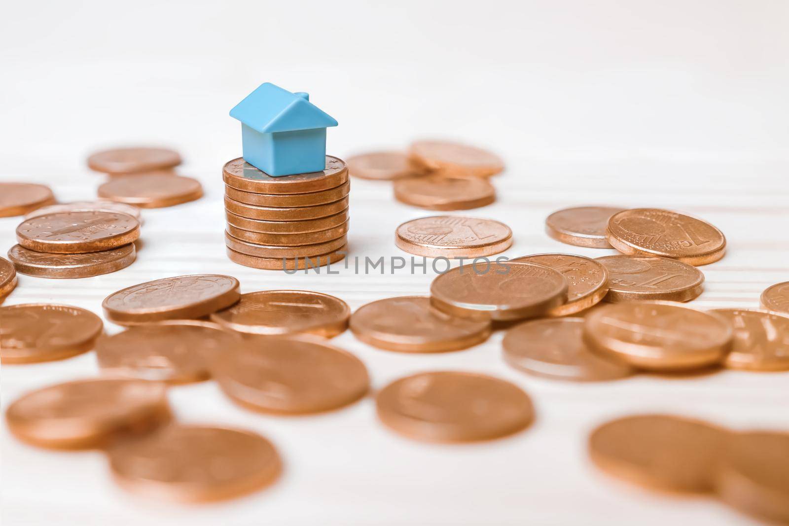 One euro cent stack coins pile with miniature house investment property market on white wood background. Toy blue model house mortgage rates income real estate rental home invest money loan property