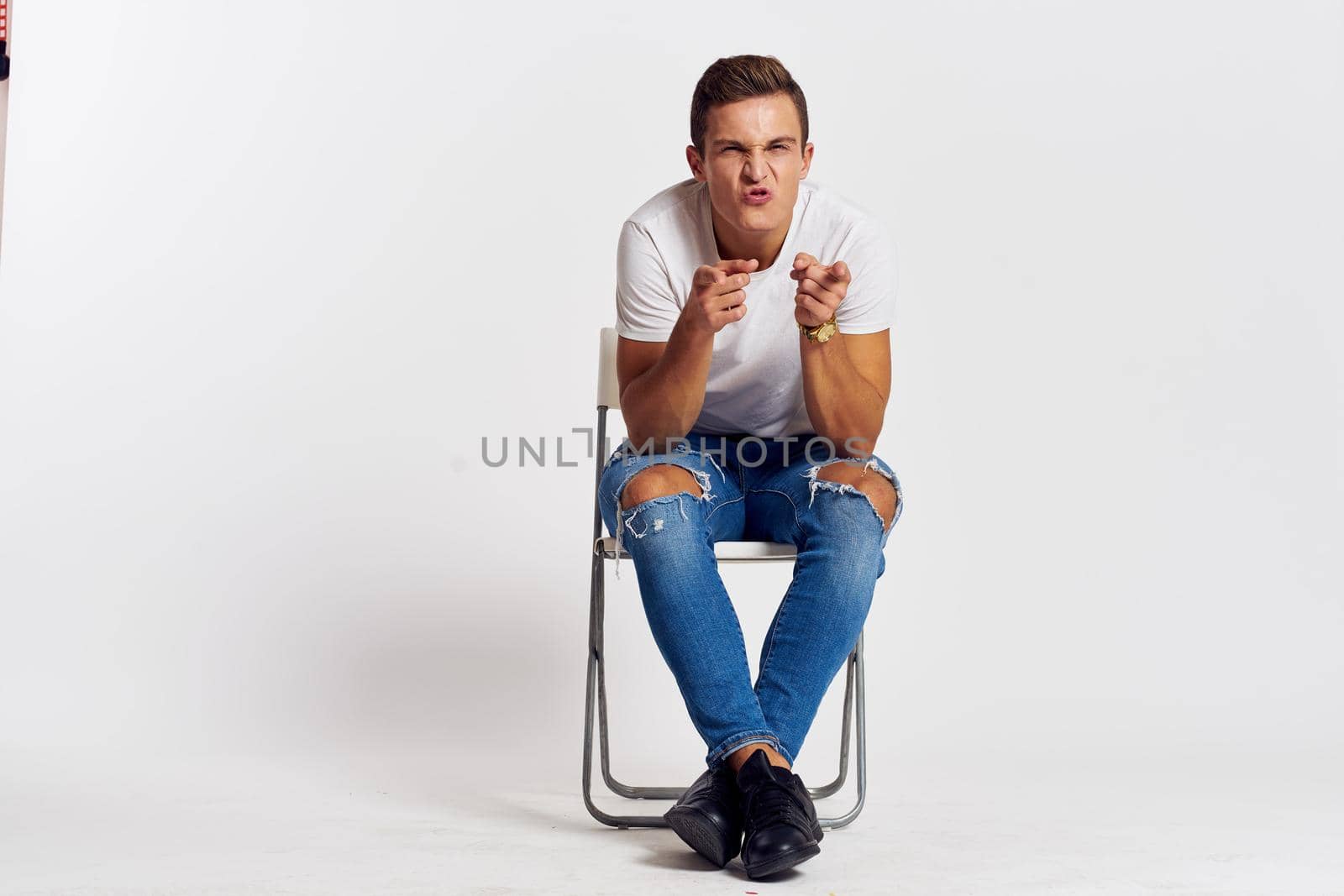 Man on a chair indoors torn jeans white t-shirt handsome face model light background. High quality photo