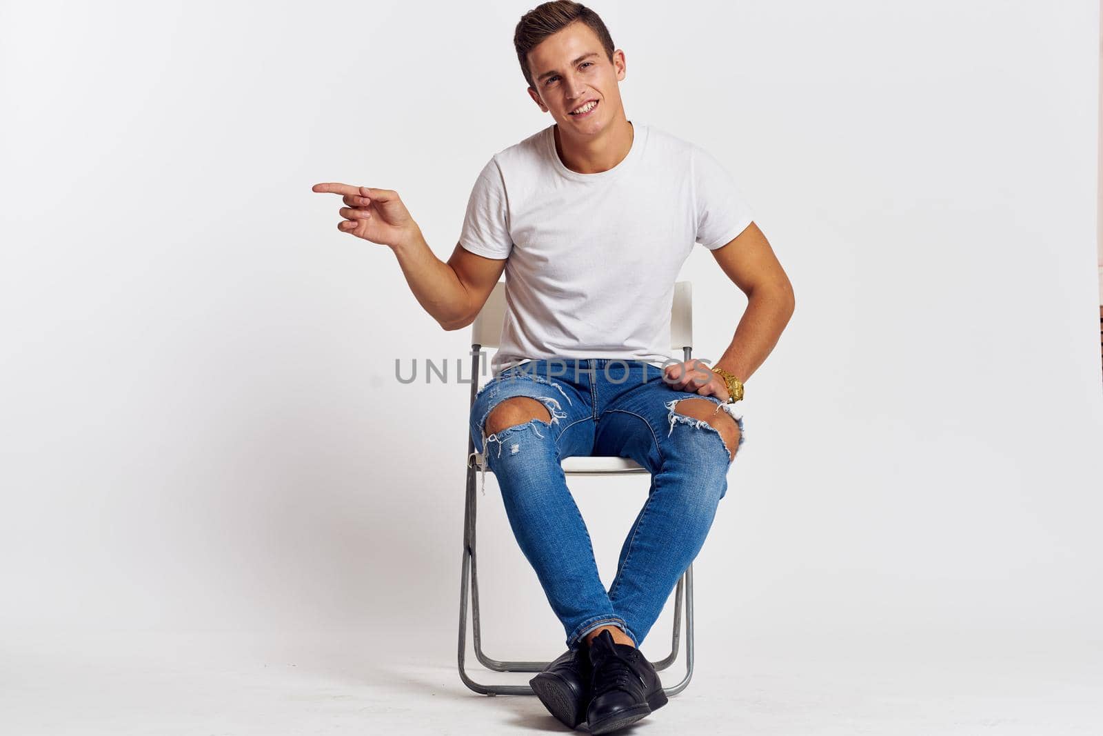 Man on a chair indoors torn jeans white t-shirt handsome face model light background by SHOTPRIME