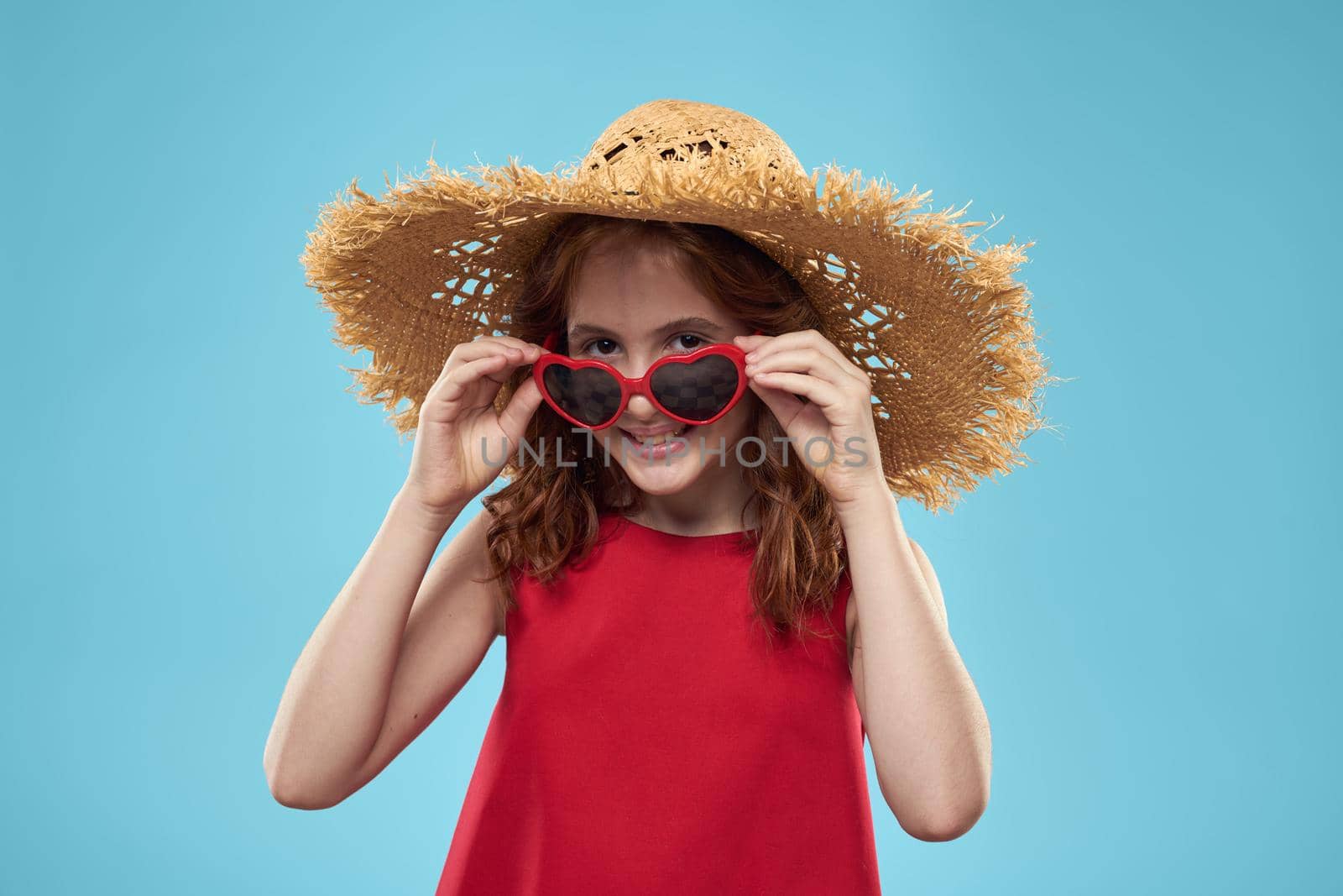 Girl in a beach Straw hat in sunglasses curly hair fun blue background. High quality photo