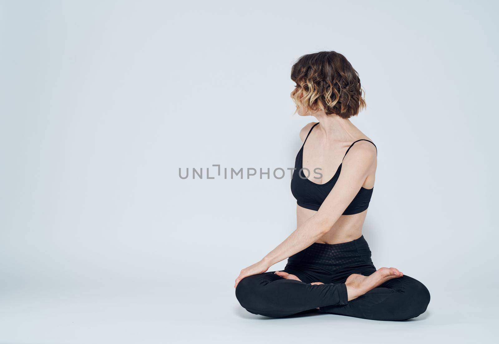 A woman in leggings sits cross-legged on the floor and turns to the sides. High quality photo