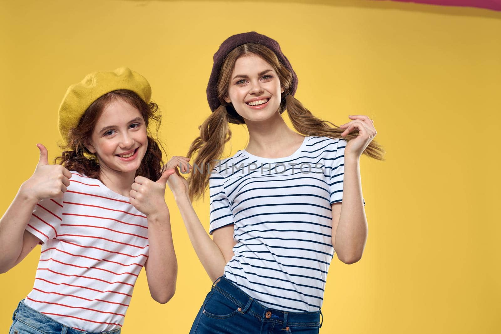 Cheerful sisters in hats striped T-shirts joy lifestyle yellow background family by SHOTPRIME