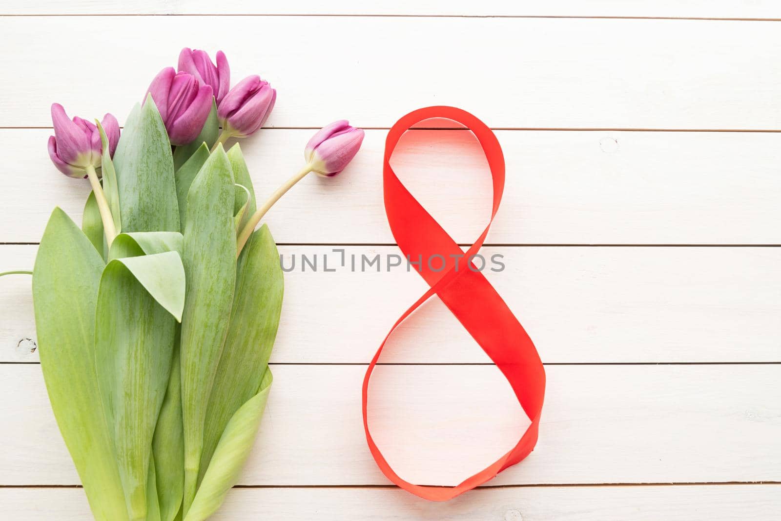 Purple tulips and red number eight for international womens day over white wooden table background with copy space