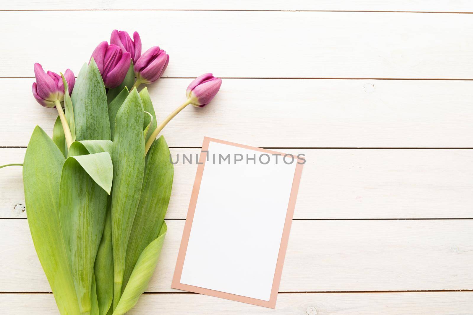 White card or menu card with spring tulips top view over white wooden background. Mock up design.