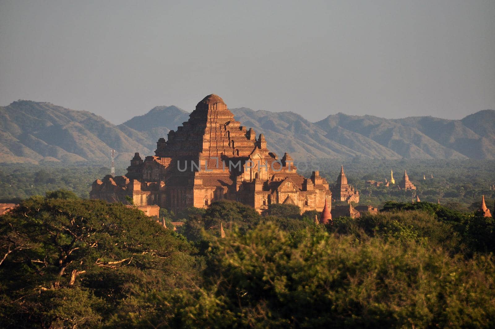 BAGAN, MYANMAR - NOVEMBER 18, 2015: Ancient oriental temple in green terrain, View of beautiful stone Dhammayangyi in green spacious terrain, mountains on background. Mingalazedi Sulamani Shwezigon