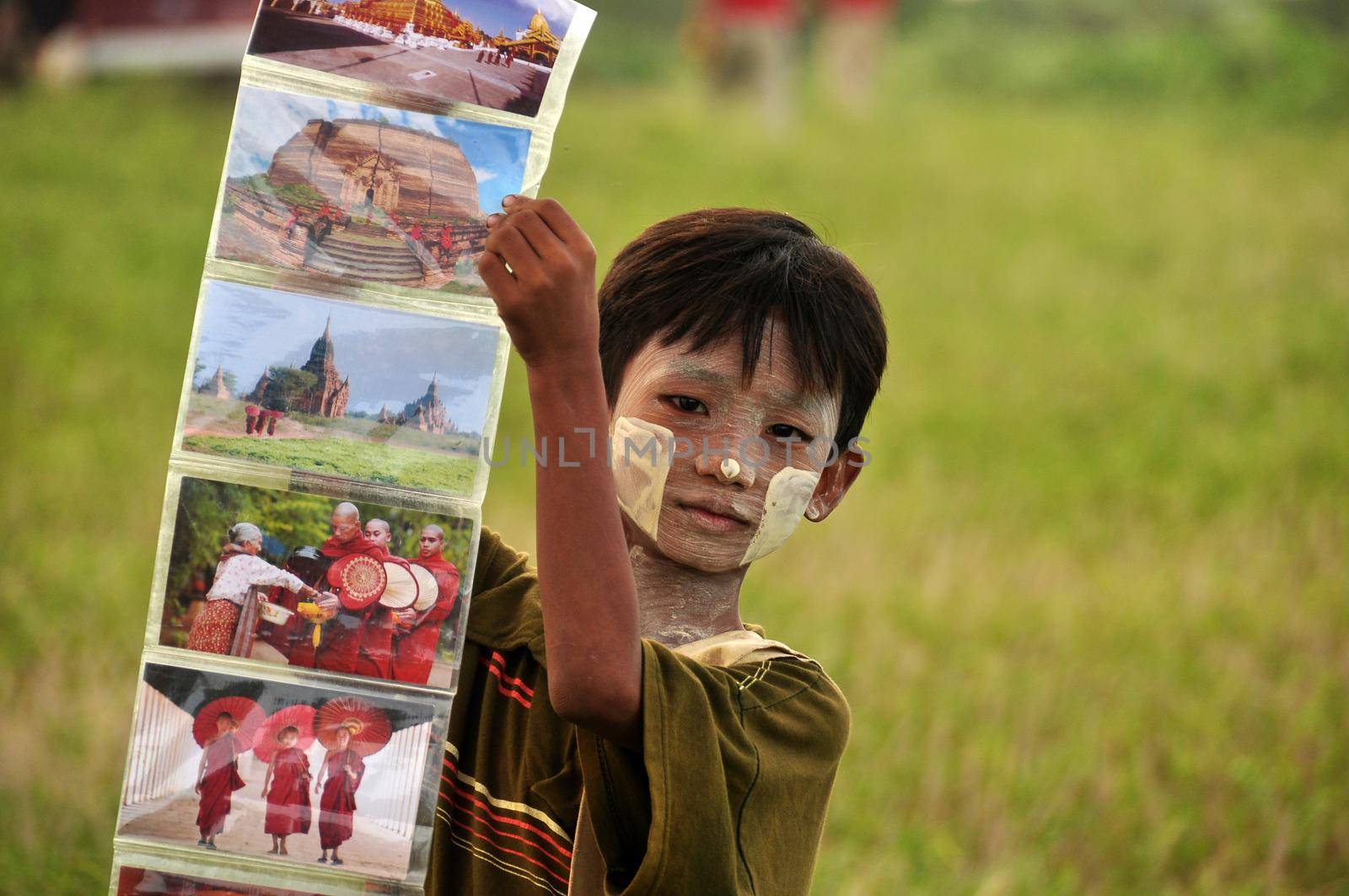 BAGAN, MYANMAR - NOVEMBER 18, 2015: Little ethnic boy showing colorful photos, Cute Asian boy with face paint in tanaka showing collage of colorful photos of oriental culture. Traditional look