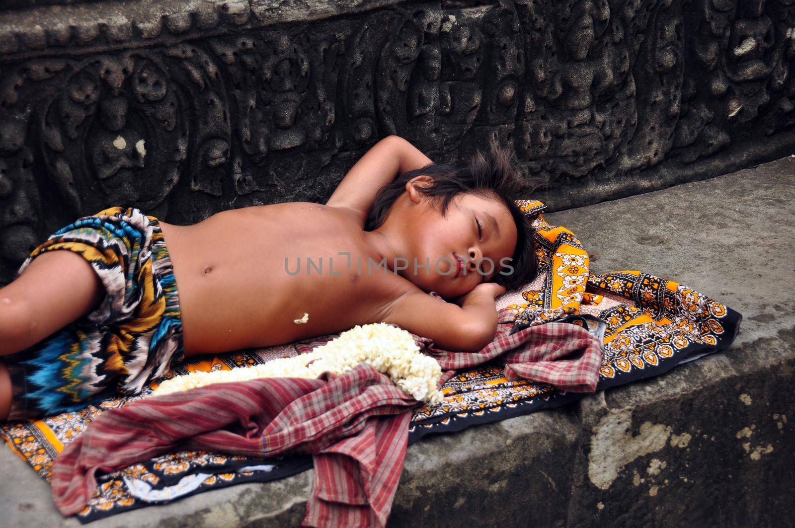 ANGKOR, CAMBODIA - AUG 28, 2013: Sleeping ethnic boy on step of temple, Little ethnic boy sleeping on ornamental rug on stone step of ancient Angkor Wat temple. Mowgli