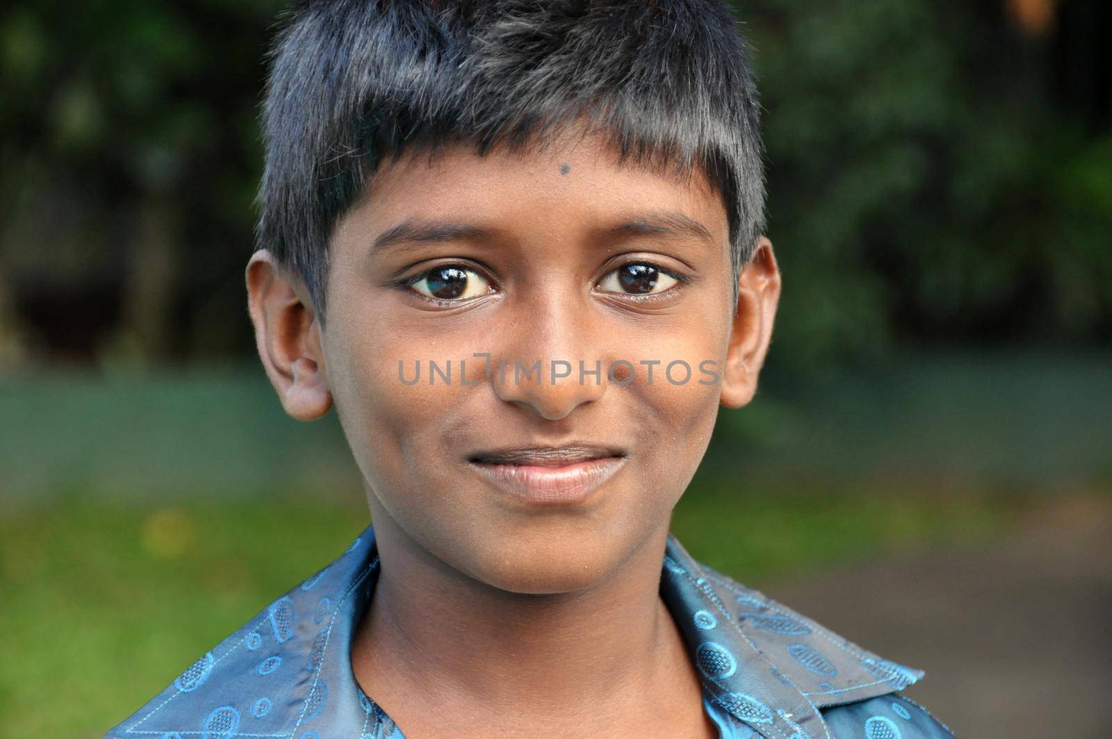 KANDY, SRI LANKA - 17th DEC, 2011: Young smiling ethnic boy looking at camera, Portrait of young smiling Indian boy in blur shirt looking at camera in nature.