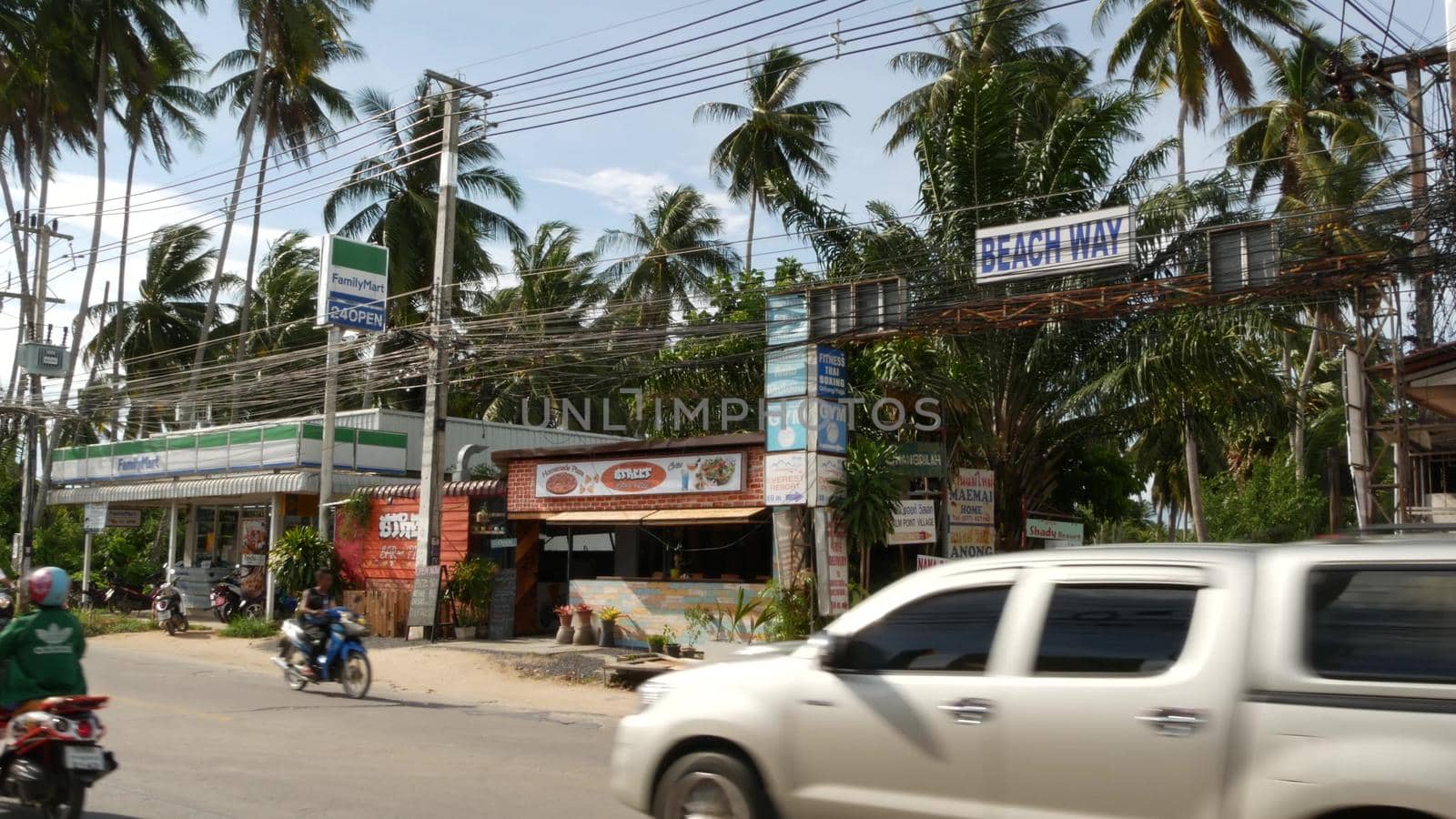 KOH SAMUI ISLAND, THAILAND - 24 JUNE 2019 Driving cars and small shops on roadside. Beach way and chain store Family mart on main road. Typical touristic village street. Thai people on motorbikes