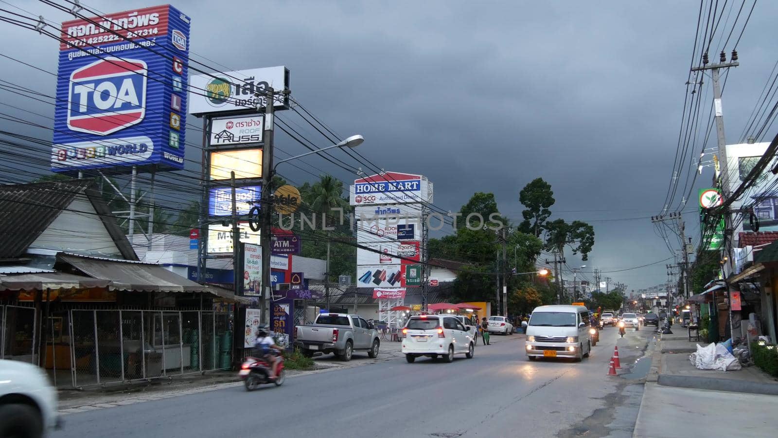KOH SAMUI ISLAND, THAILAND - 21 JUNE 2019 Busy transport populated city street in cloudy day. Typical street full of motorcycles and cars. Thick blue clouds before storm during wet season. by DogoraSun
