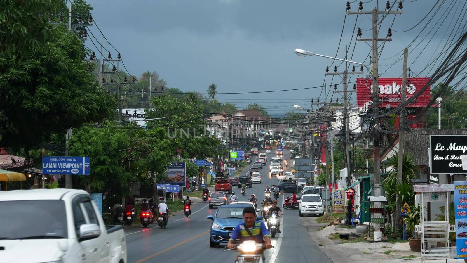 KOH SAMUI ISLAND, THAILAND - 11 JULY 2019 Busy transport populated city street in cloudy day. Typical street full of motorcycles and cars. Thick blue clouds before storm during wet season. by DogoraSun