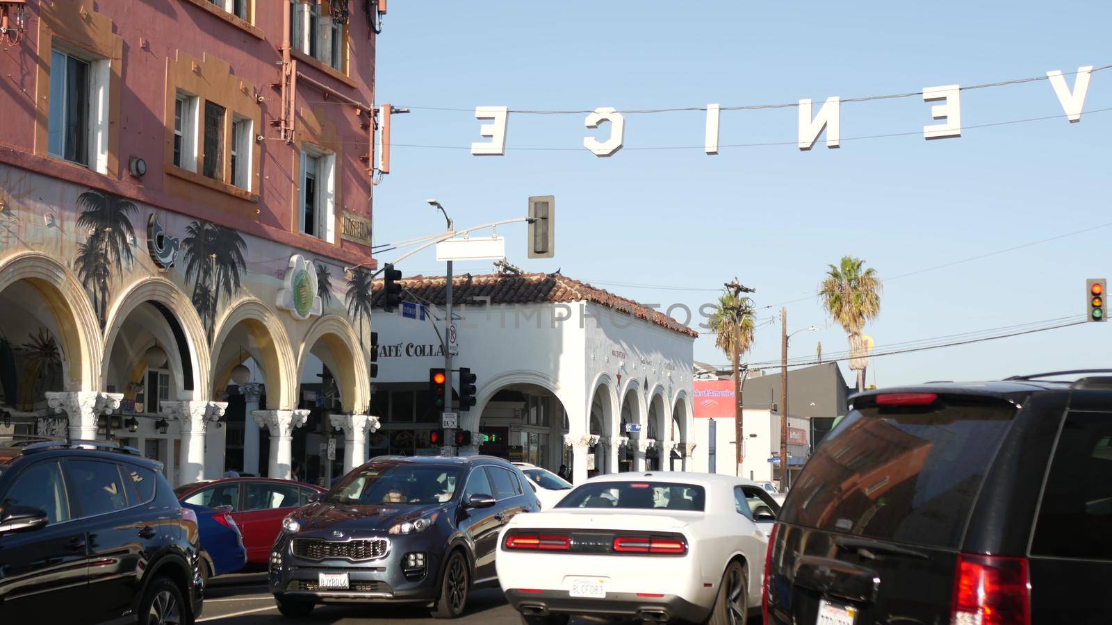 LOS ANGELES CA USA - 16 NOV 2019: California summertime Venice beach aesthetic. Iconic retro sign hanging on street. Famous symbol and travel destination. Letters over the road with cars and people by DogoraSun