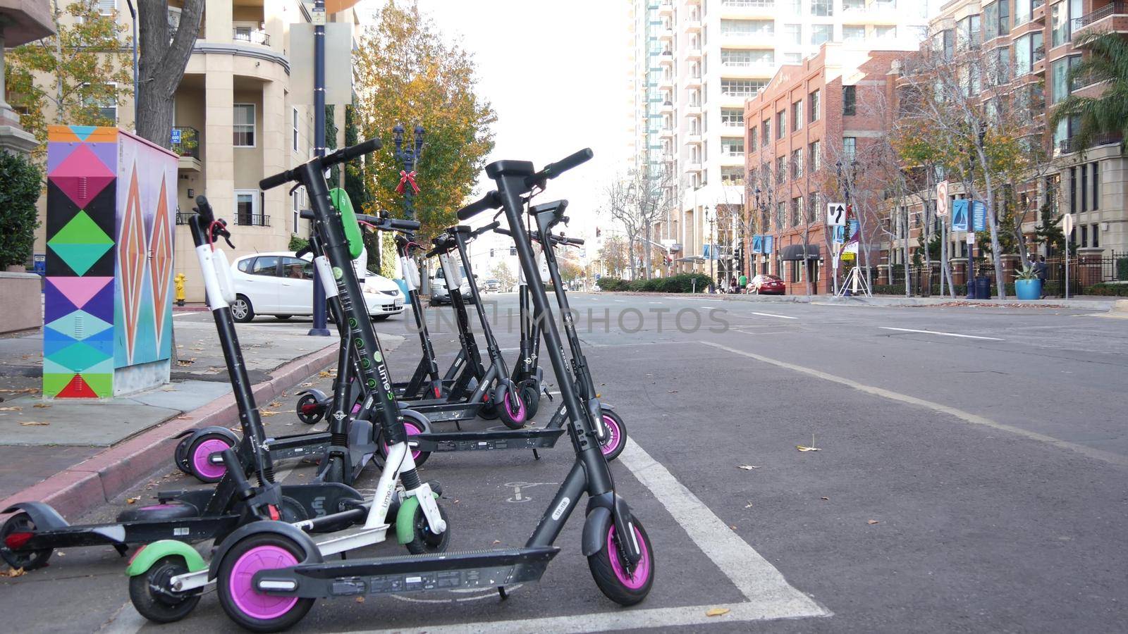SAN DIEGO, CALIFORNIA USA - 4 JAN 2020: Row of ride sharing electric scooters parked on street in Gaslamp Quarter. Rental dockless public bikes, eco transport in city. Rent kick cycle with mobile app by DogoraSun
