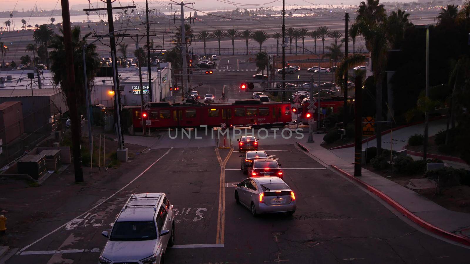 SAN DIEGO, CALIFORNIA USA - 15 JAN 2020: Level crossing near Lindbergh field international airport. Railroad tram and runway at sunset. MTS Trolley rail transportation, cars and railway transport.