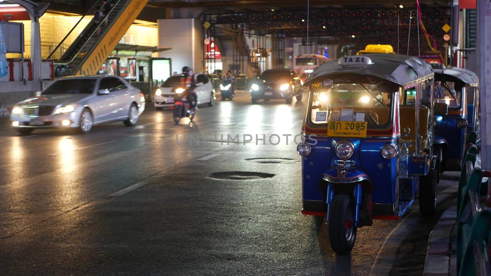 BANGKOK, THAILAND - 18 DECEMBER, 2018: Traditional Thai taxi - Tuk Tuk awaits tourists along the road. Night traffic of overpopulated city. Symbol of asian country, unique vehicle.