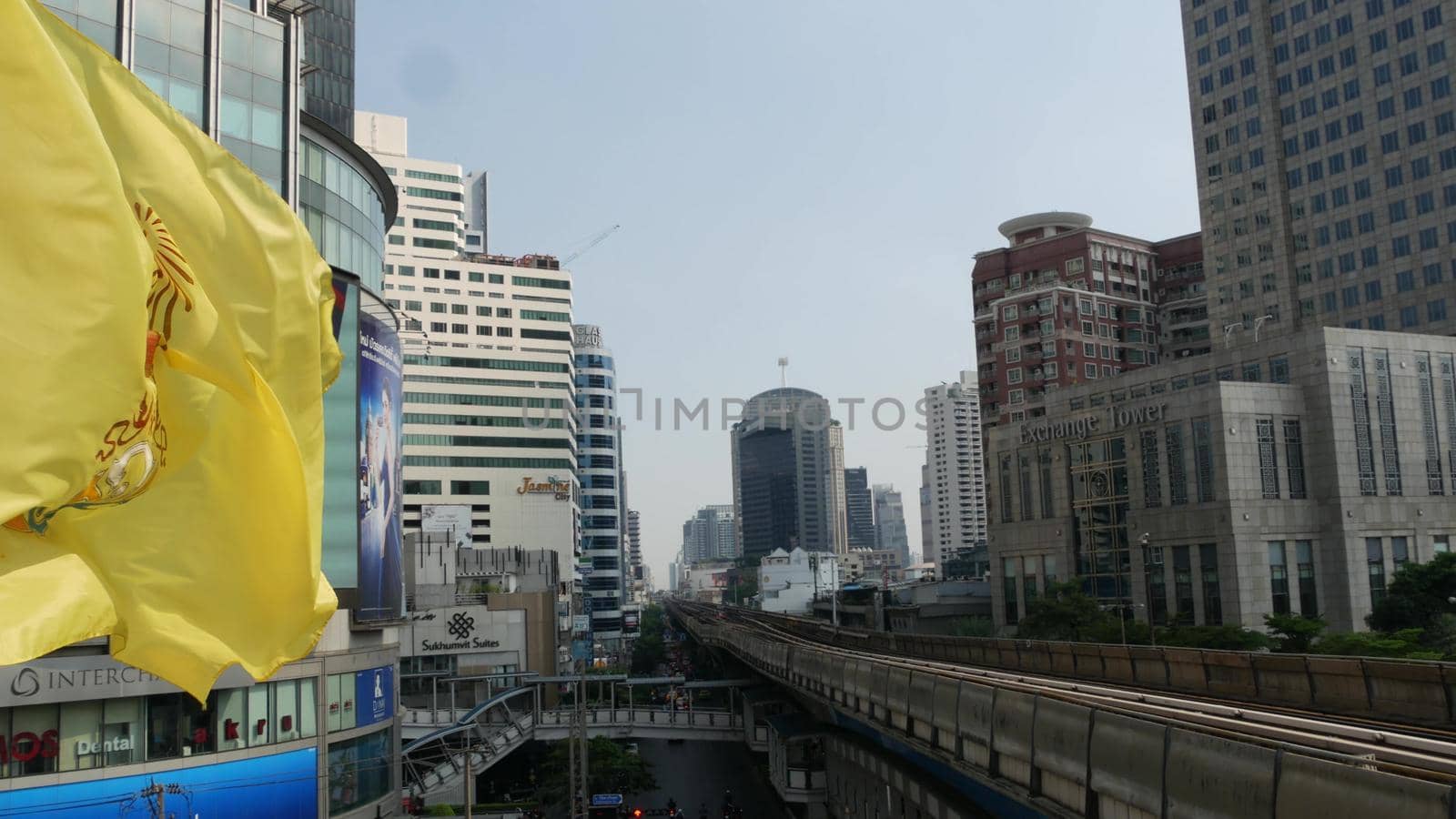 BANGKOK, THAILAND - 18 DECEMBER, 2018: Train riding on city street. Modern train riding on railway bridge over road with cars on amazing modern street. Royal yellow flag fluttering in the wind.