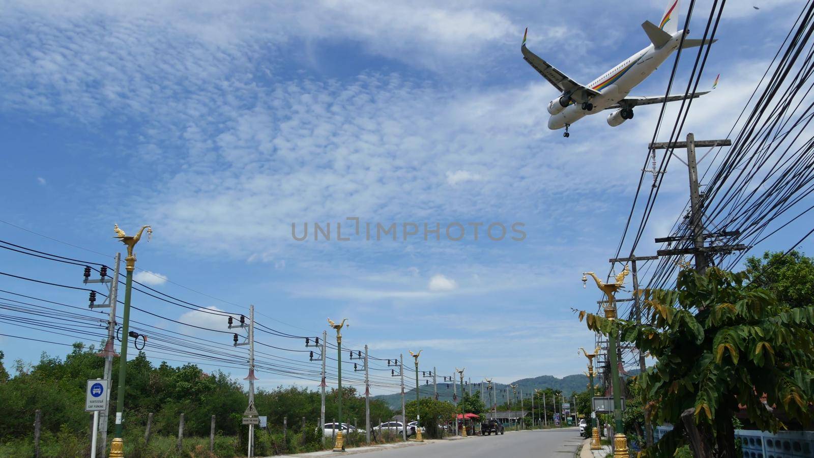 KOH SAMUI ISLAND, THAILAND - 23 JUNE 2019 Plane landing over typical main road street of tropical town. Aircraft flying to Bangkok airways airport, exotic touristic resort. Thai people on motorbikes