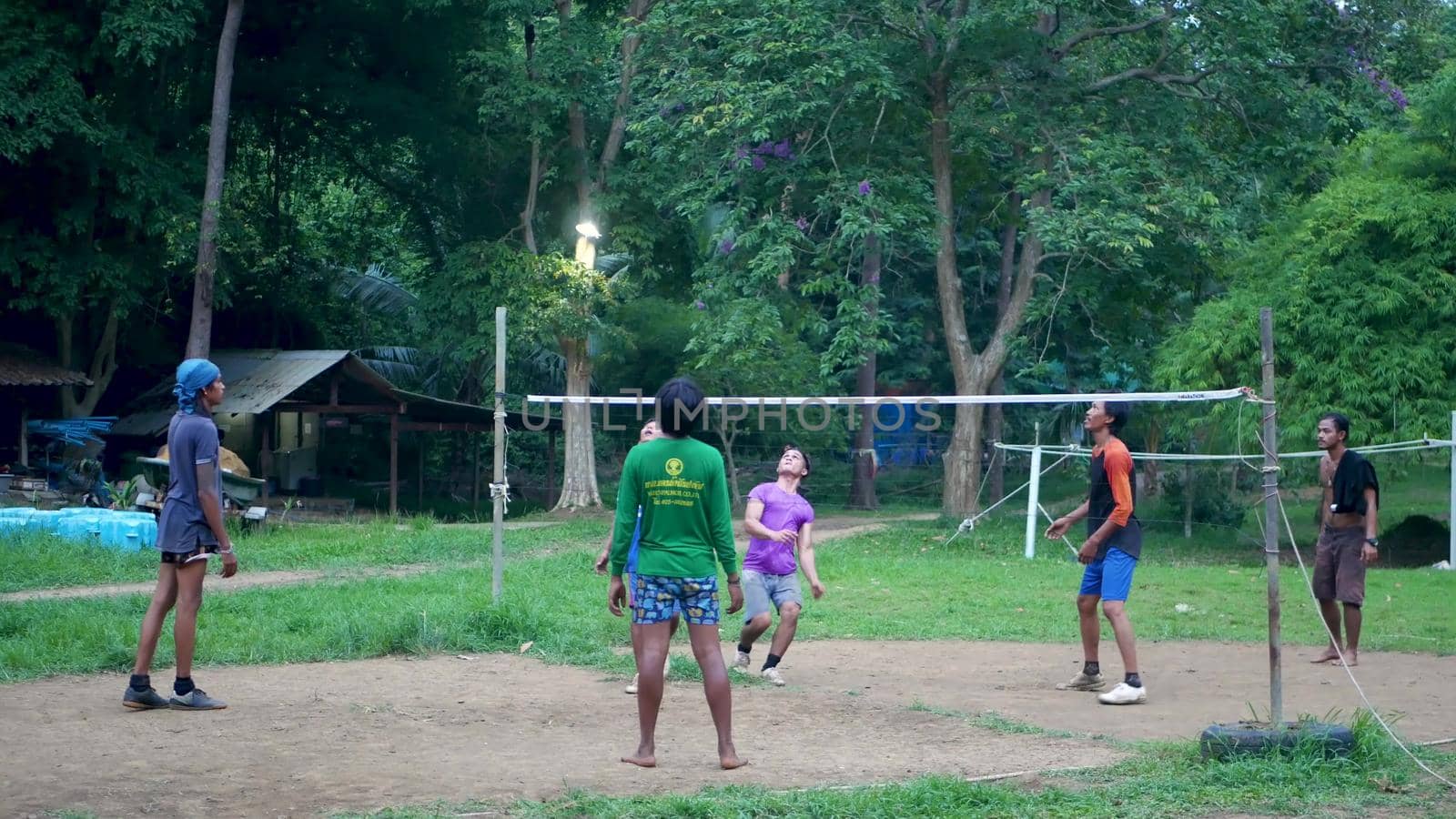 ANG THONG, THAILAND - 9 JUNE 2019: Thai teenagers playing sepak takraw in park. Group of men playing kick volleyball against green trees in yard in local settlement. Traditional national sport game by DogoraSun
