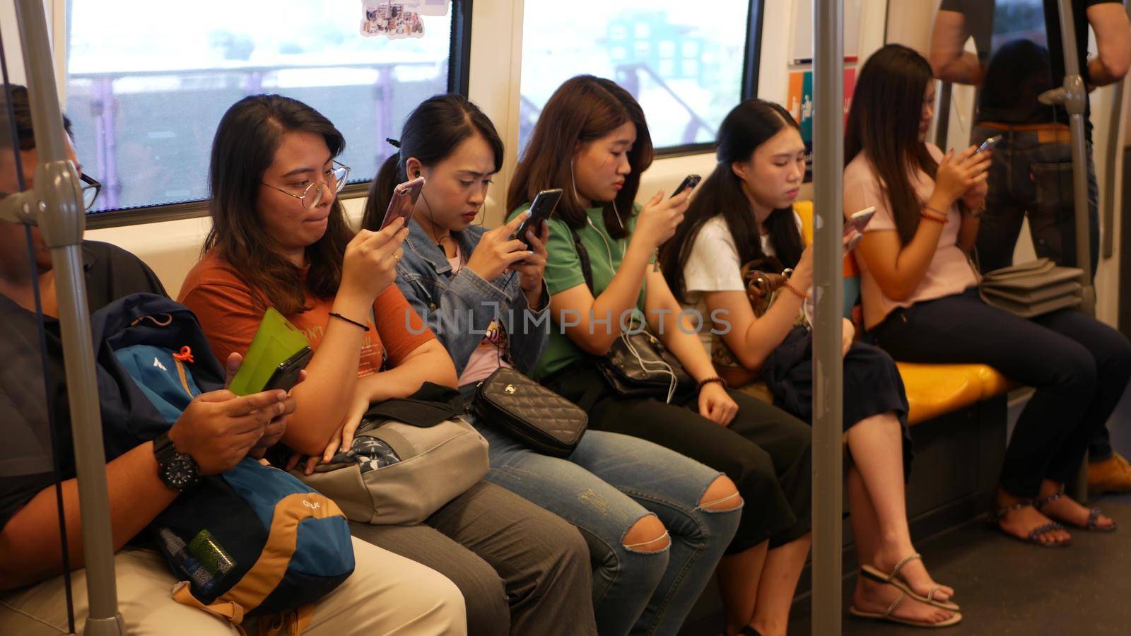 BANGKOK, THAILAND - 13 JULY, 2019: Asian passengers in train using smartphones. Thai people online surfing internet in bts car. Public transportation. Addiction from social media and phone in subway. by DogoraSun