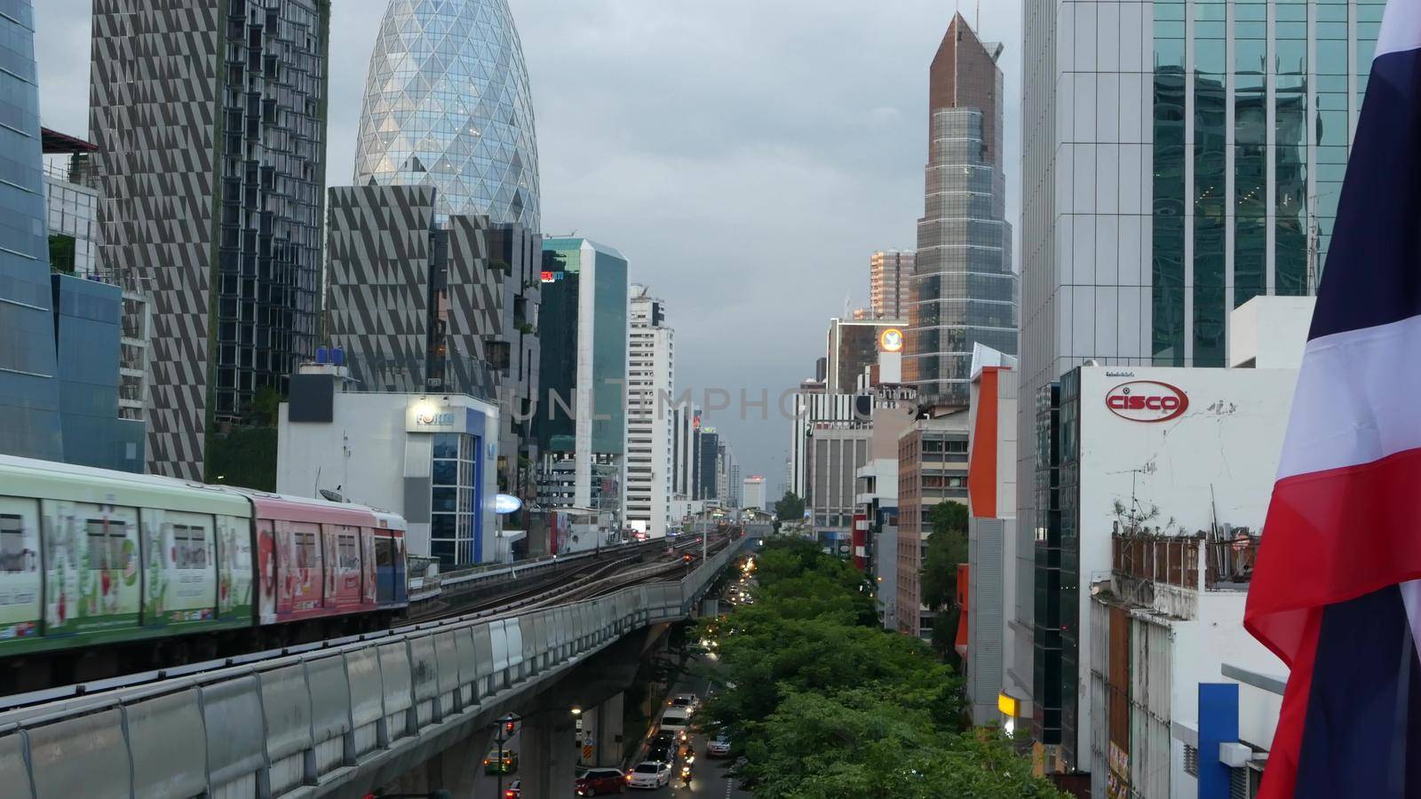 BANGKOK, THAILAND - 10 JULY, 2019: View of modern asian city from bts sky train platform. Train on metro rail road station. Public transportation in Krungtep downtown. State national flag waving. by DogoraSun