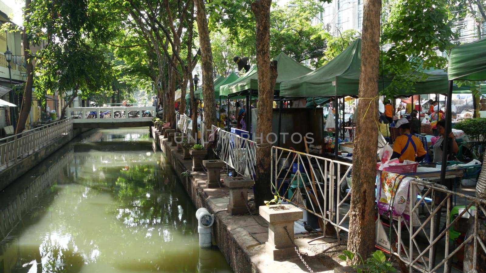 BANGKOK, THAILAND - 11 JULY, 2019: Street city life near river canal in siam. Traditional khlong with bridge near local market. Thai people on the riverside. Classic water way in Krungtep. by DogoraSun