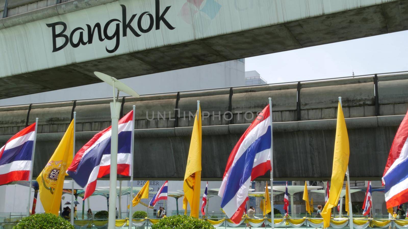 BANGKOK, THAILAND - 11 JULY, 2019: Pedestrians walking on the bridge near MBK and Siam Square under BTS train line. People in festive modern city decorated with waving national flags and royal symbol by DogoraSun