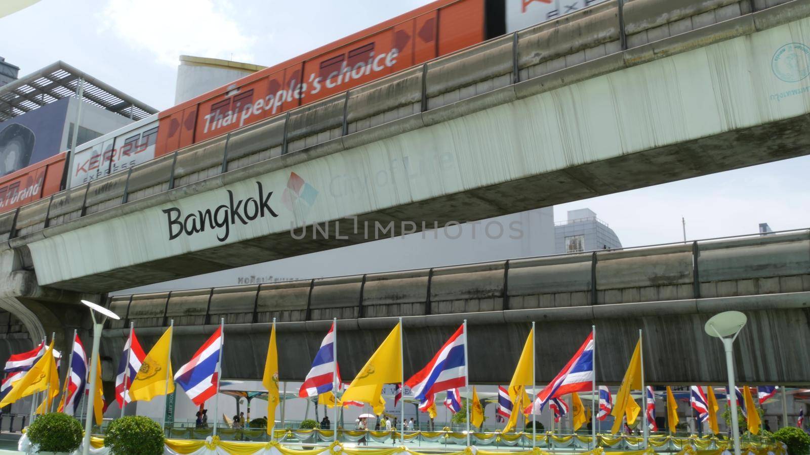 BANGKOK, THAILAND - 11 JULY, 2019: Pedestrians walking on the bridge near MBK and Siam Square under BTS train line. People in festive modern city decorated with waving national flags and royal symbol.