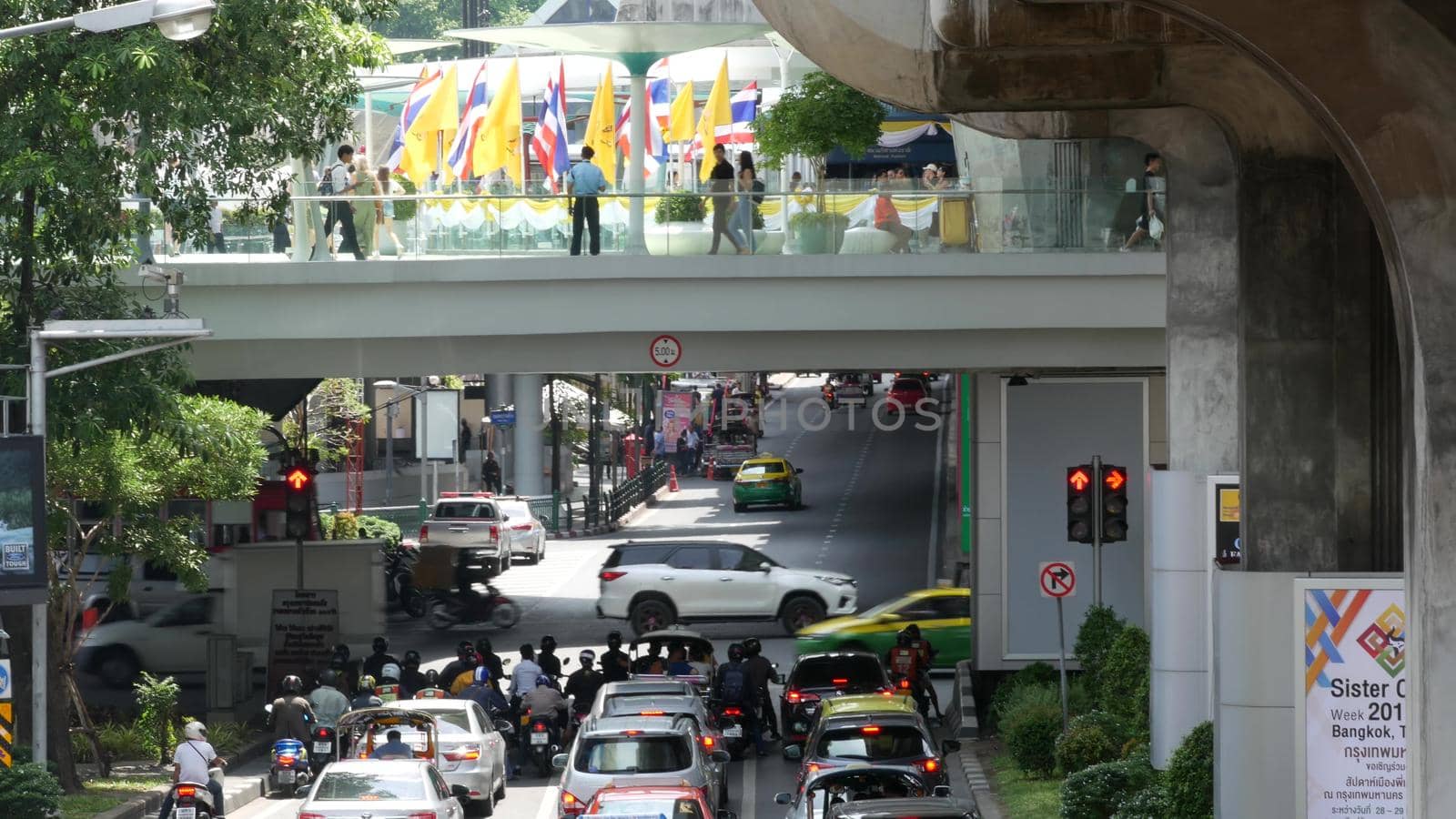 BANGKOK, THAILAND - 11 JULY, 2019: Intersection on busy city street. People on motorcycles and cars riding on crossroad under pedestrian bridge on busy street