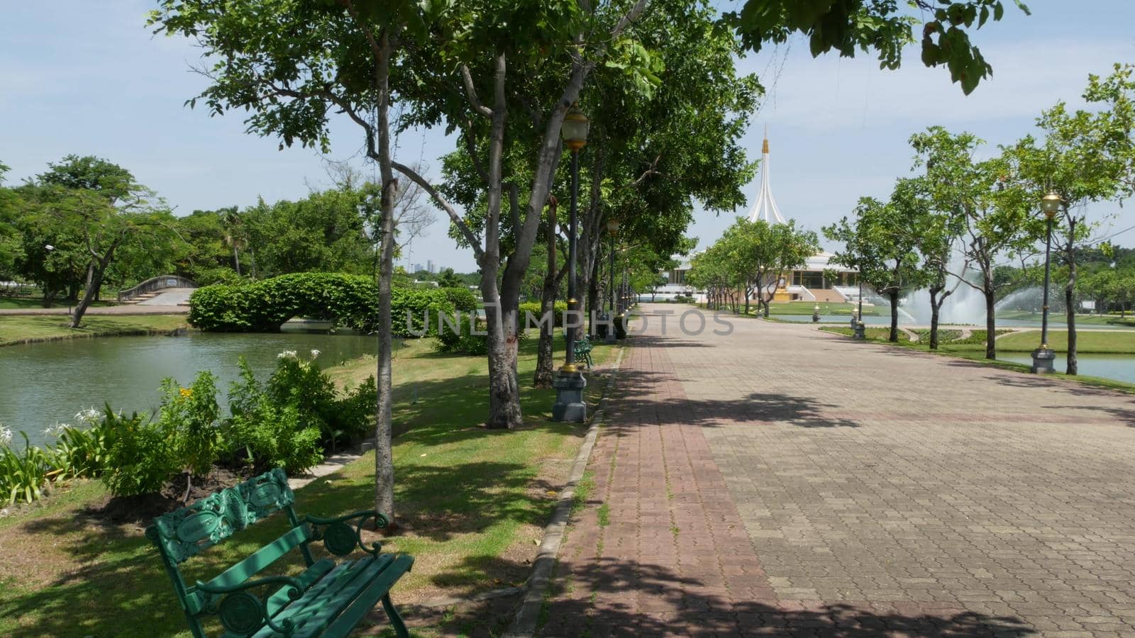 BANGKOK, THAILAND - 12 JULY, 2019: Blooming garden near pavilion in park. Green trees and flowers growing near pavilion building against cloudless blue sky on sunny day in King Rama IX Park