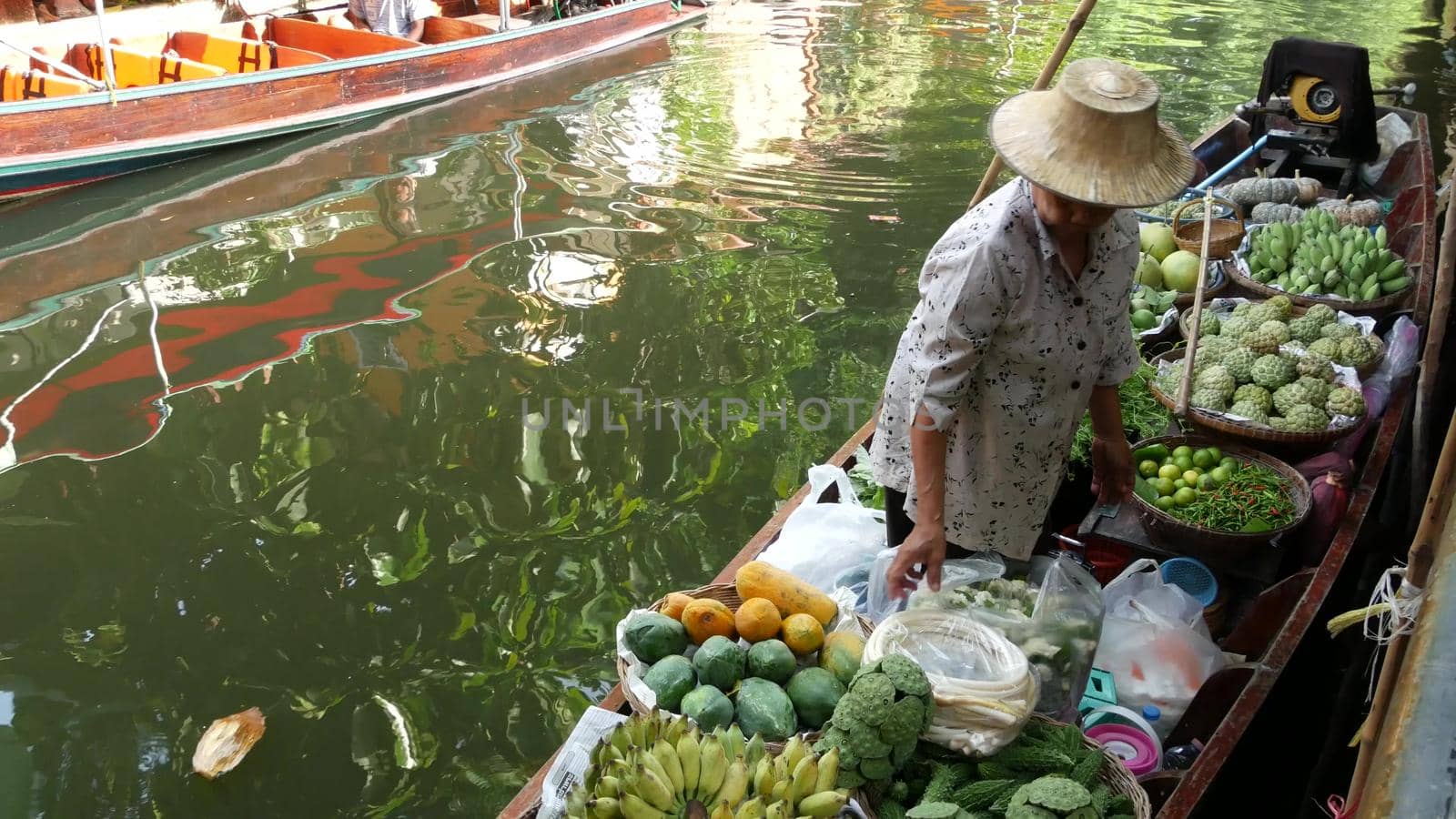 BANGKOK, THAILAND - 13 JULY 2019: Lat Mayom floating market. Traditional classic khlong river canal, local women farmers, long-tail boats with fruits and vegetables. Iconic asian street food selling