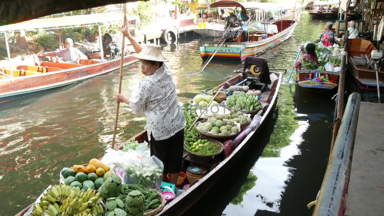 BANGKOK, THAILAND - 13 JULY 2019: Lat Mayom floating market. Traditional classic khlong river canal, local women farmers, long-tail boats with fruits and vegetables. Iconic asian street food selling. by DogoraSun