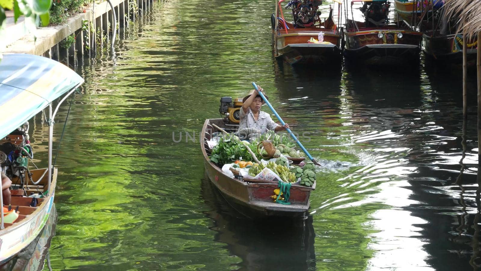 BANGKOK, THAILAND - 13 JULY 2019: Lat Mayom floating market. Traditional classic khlong river canal, local women farmers, long-tail boats with fruits and vegetables. Iconic asian street food selling. by DogoraSun