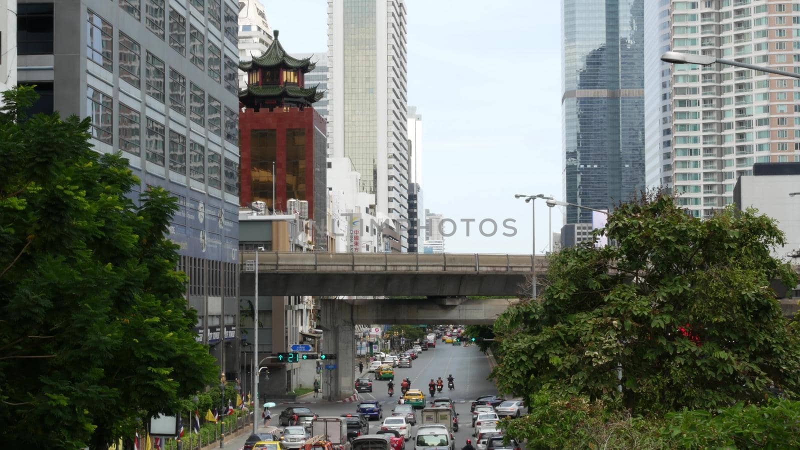 BANGKOK, THAILAND - 13 JULY, 2019: Traffic on modern city street. Contemporary train riding on railroad bridge over road with cars in center of capital. by DogoraSun