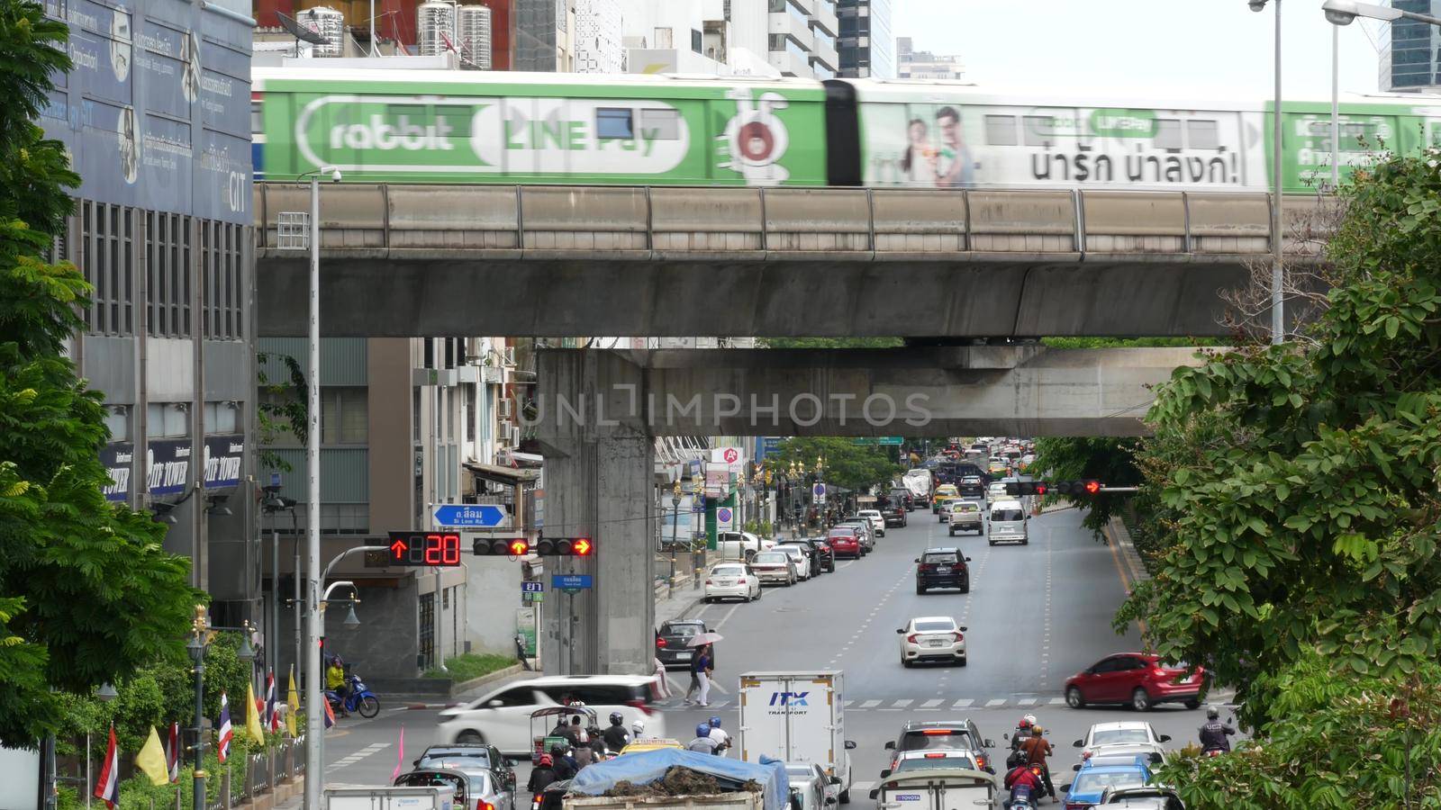 BANGKOK, THAILAND - 13 JULY, 2019: Traffic on modern city street. Contemporary train riding on railroad bridge over road with cars in center of capital. by DogoraSun